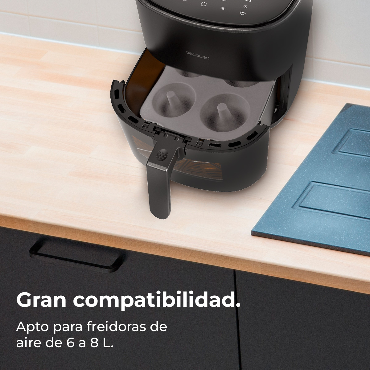 Freidora de aire negra con bandeja que muestra moldes para donas. Se encuentra sobre una encimera de madera con un armario negro debajo. Una tabla de cortar azul a un lado.