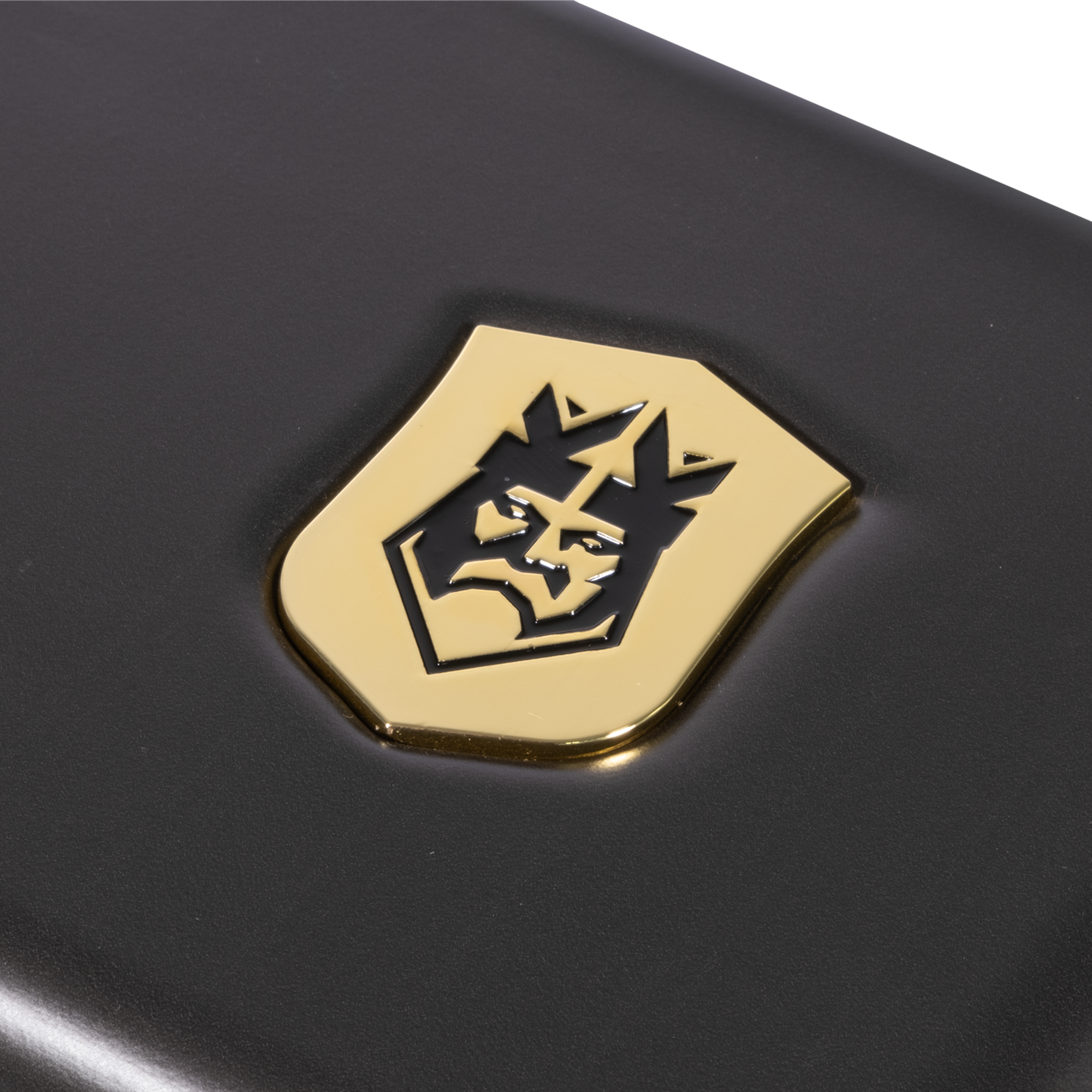 Emblema dorado con la cara de un león y corona sobre una superficie negra. El emblema es brillante y detallado.