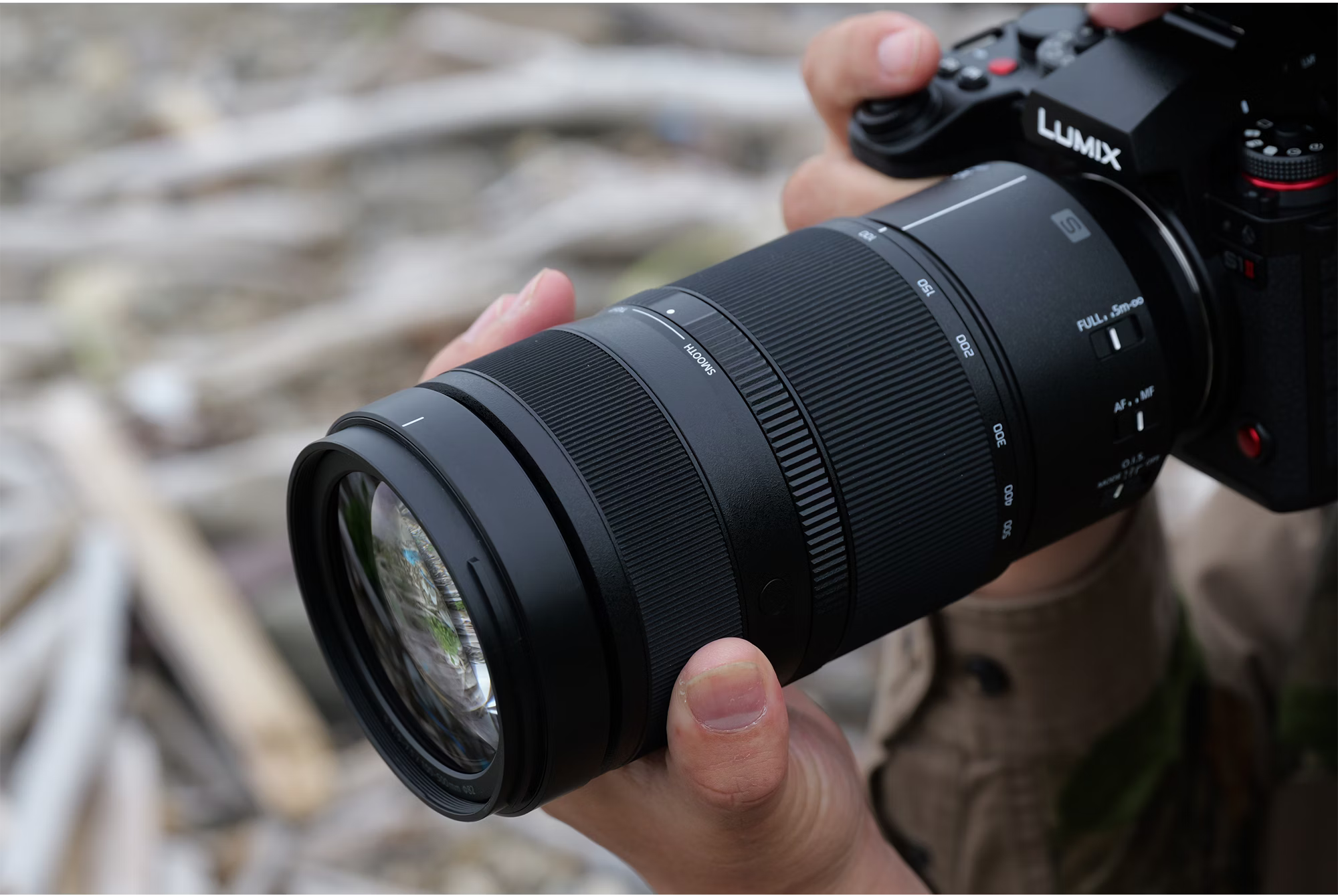 Une personne tient un appareil photo noir avec un long objectif. L'objectif a des marquages et des réglages de mise au point. Arrière-plan flou.