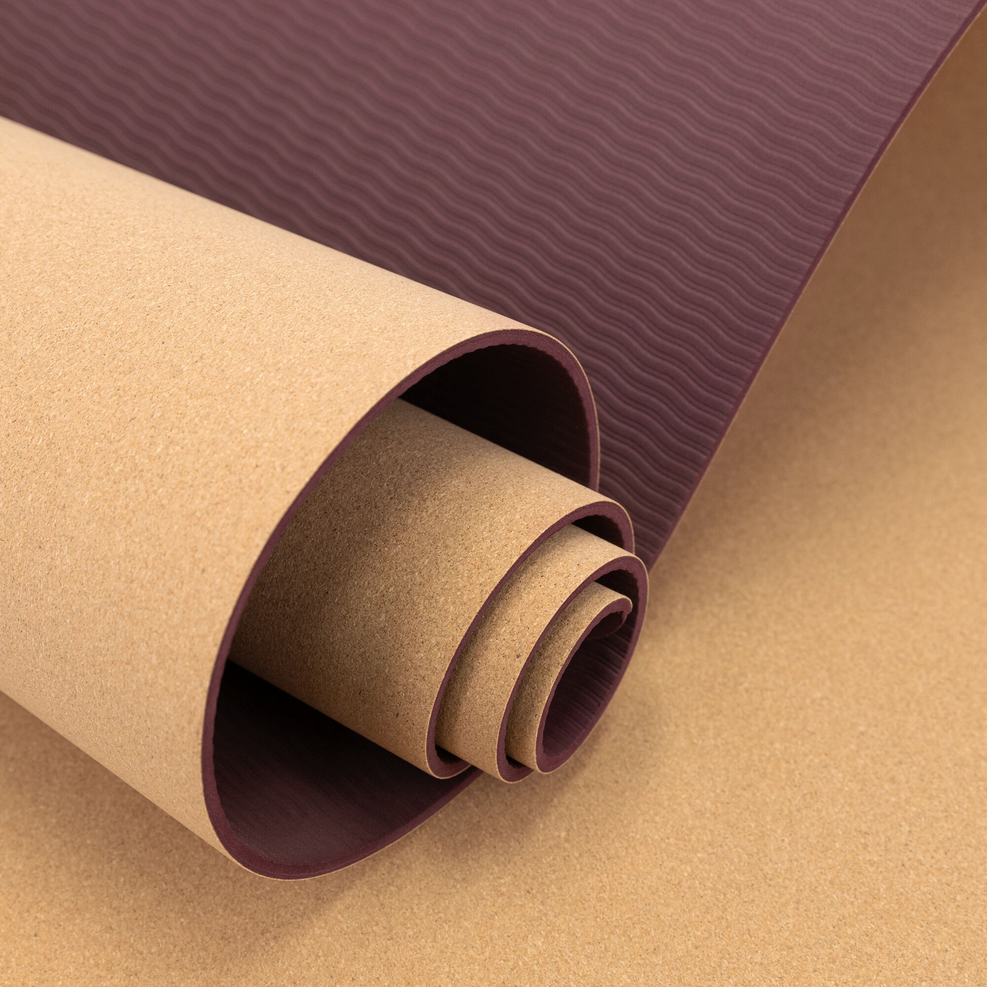Zwinięta mata do jogi z brązowym korkiem i głębokim fioletowym spodem, częściowo rozwinięta, pokazująca fakturę i warstwy.