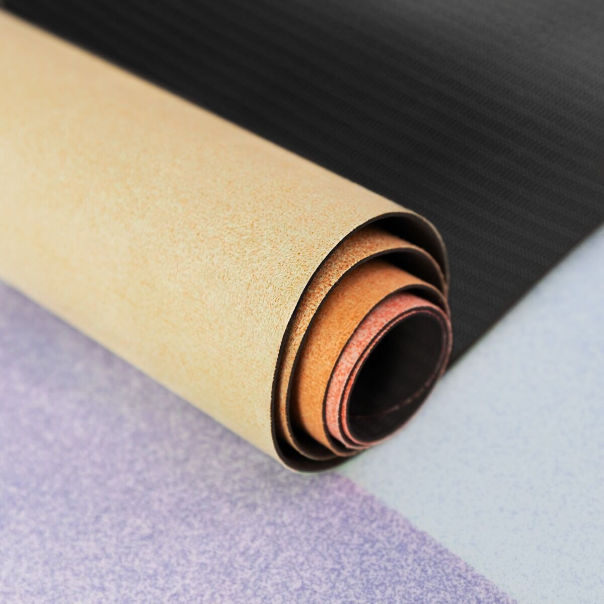 Zrolowana beżowa mata z widocznymi pomarańczowymi i czerwonymi warstwami. Czarne teksturowane tło i fioletowy wzór poniżej.