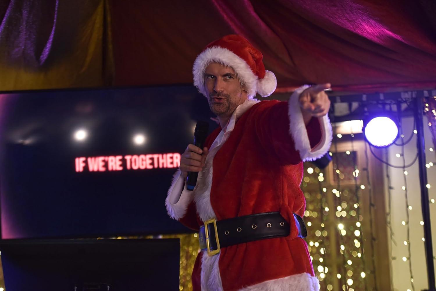 Ein als Weihnachtsmann verkleideter Mann zeigt. Er hält ein Mikrofon. Auf einem Bildschirm steht "IF WE'RE TOGETHER". Der Hintergrund umfasst Lichter.