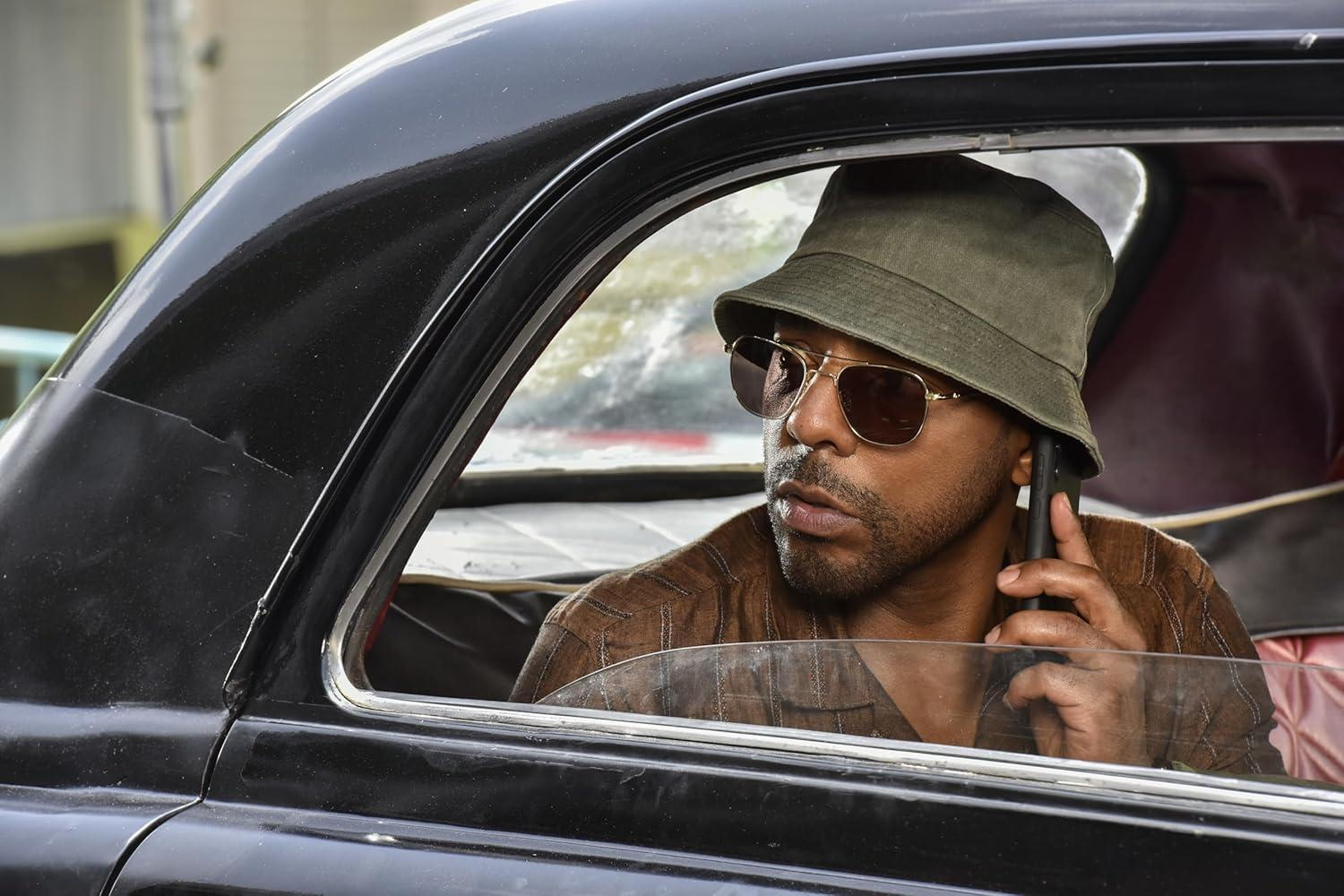 Ein Mann im Auto mit Hut und Sonnenbrille telefoniert. Das Auto ist schwarz.