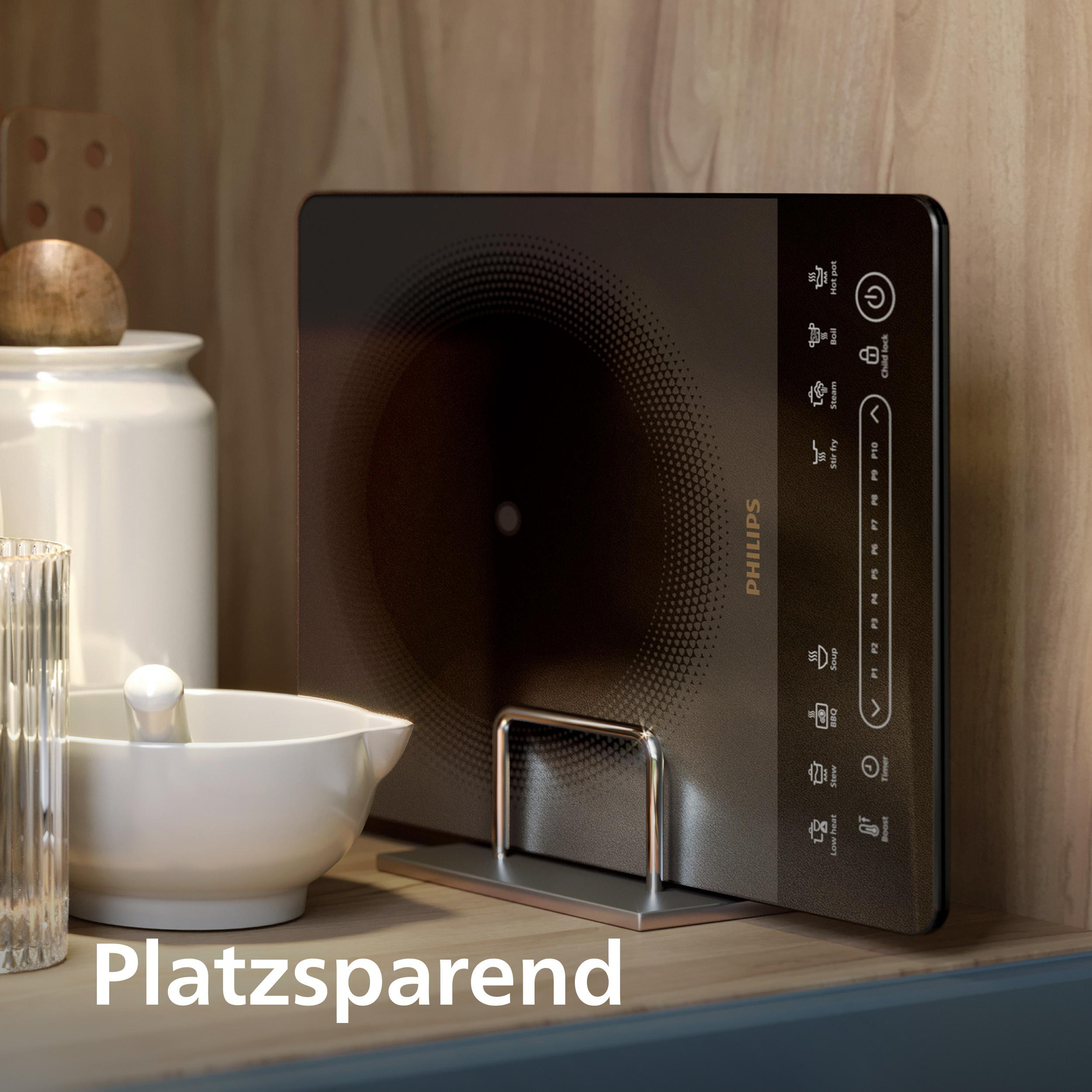 Ein Induktionskochfeld steht auf einem Regal, mit Mörser und Stößel und einem Glas. Der Text 'Platzsparend' ist sichtbar.