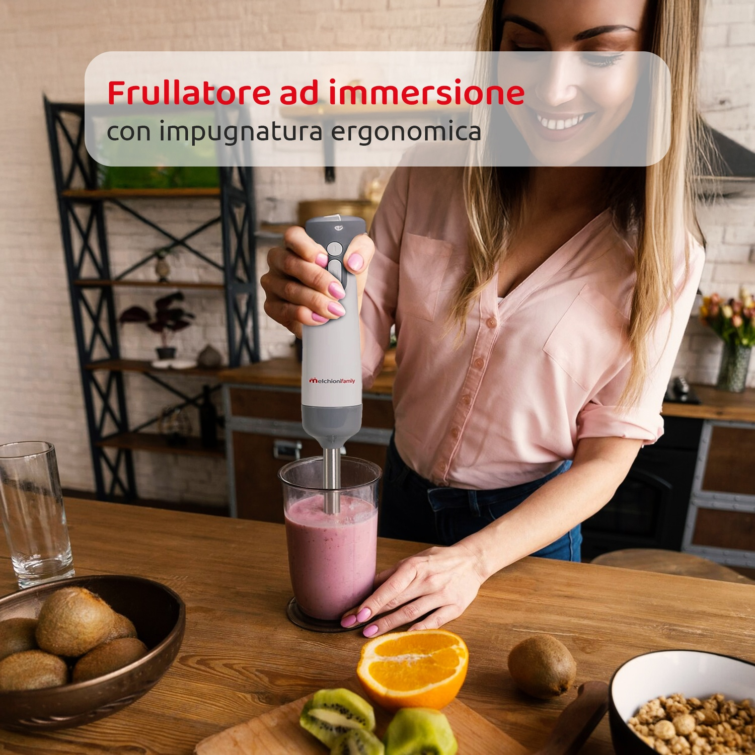 Una donna frulla un frullato rosa con un frullatore a immersione. Kiwi, arancia e una ciotola di cereali sul tavolo.