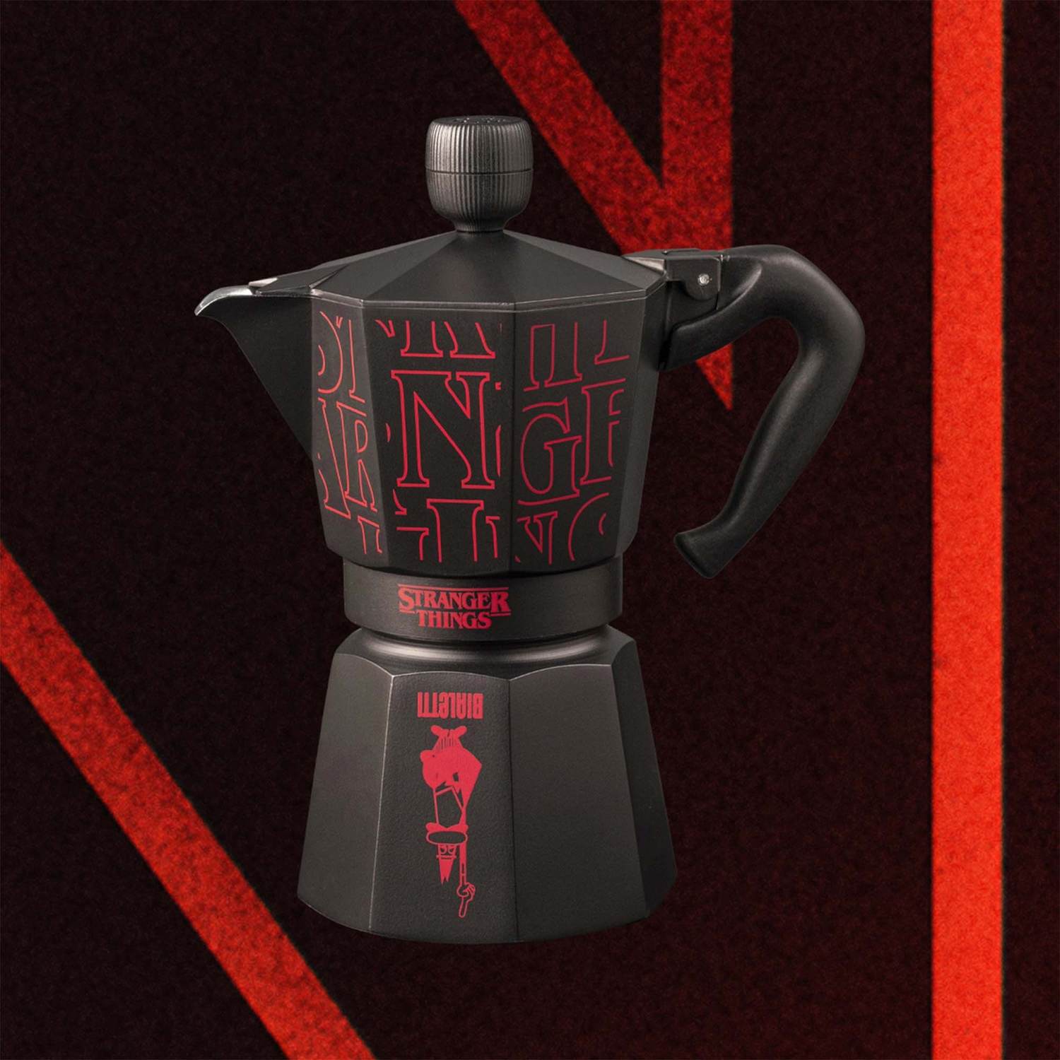 Caffettiera nera con logo rosso 'Stranger Things'. Design rosso sul corpo. Manico e coperchio neri. Lo sfondo è rosso scuro.