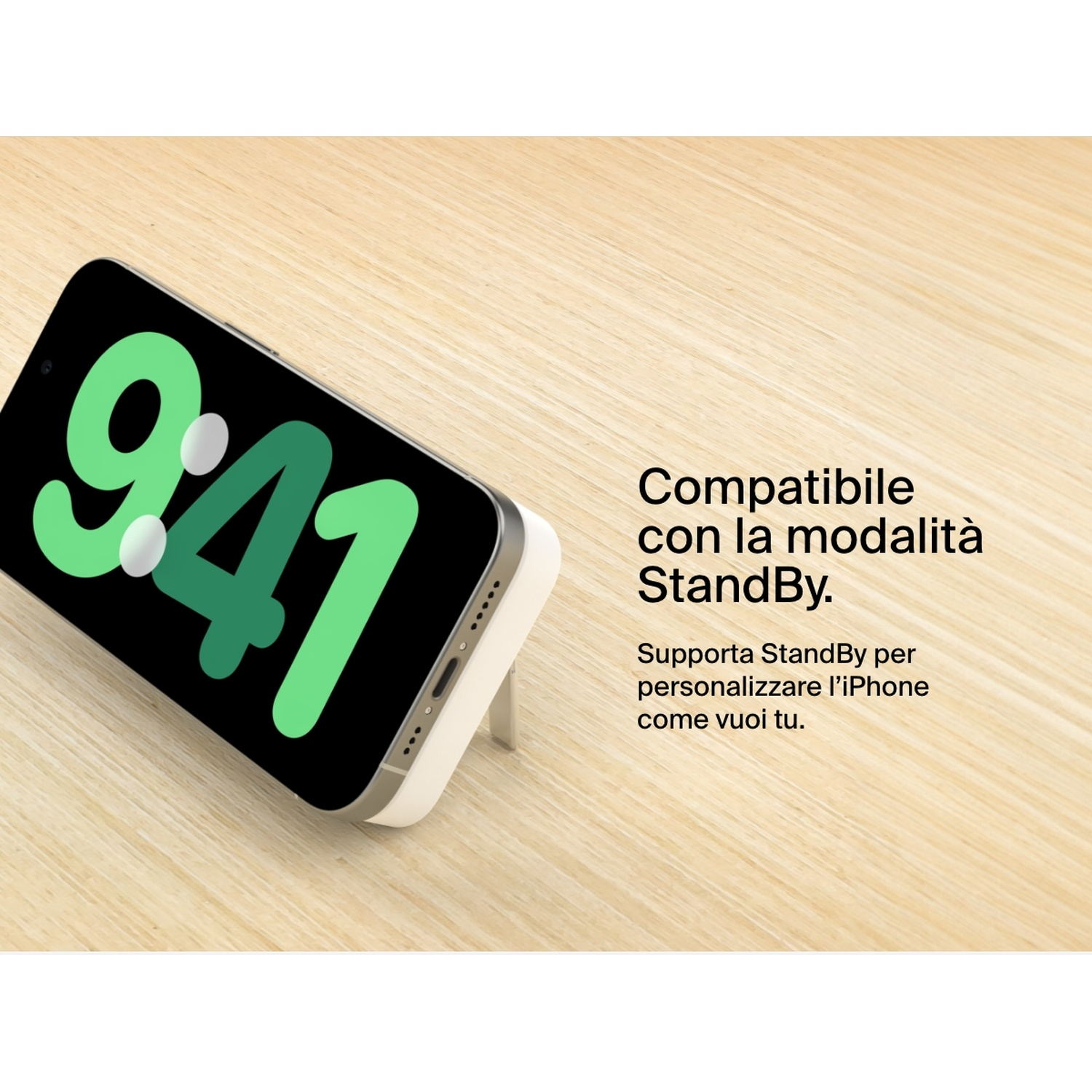 Un iPhone mostra le 9:41 sullo schermo, sorretto da un supporto bianco, su una superficie in legno, con testo sulla modalità StandBy.