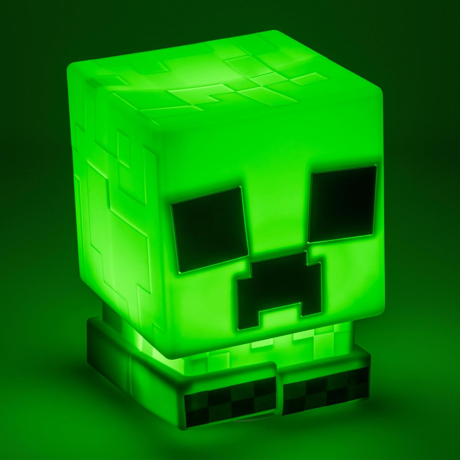 Egy zöld Creeper lámpa a Minecraft-ból, ami élénken világít. Fekete szemei és szája van, zöld alappal és háttérrel.