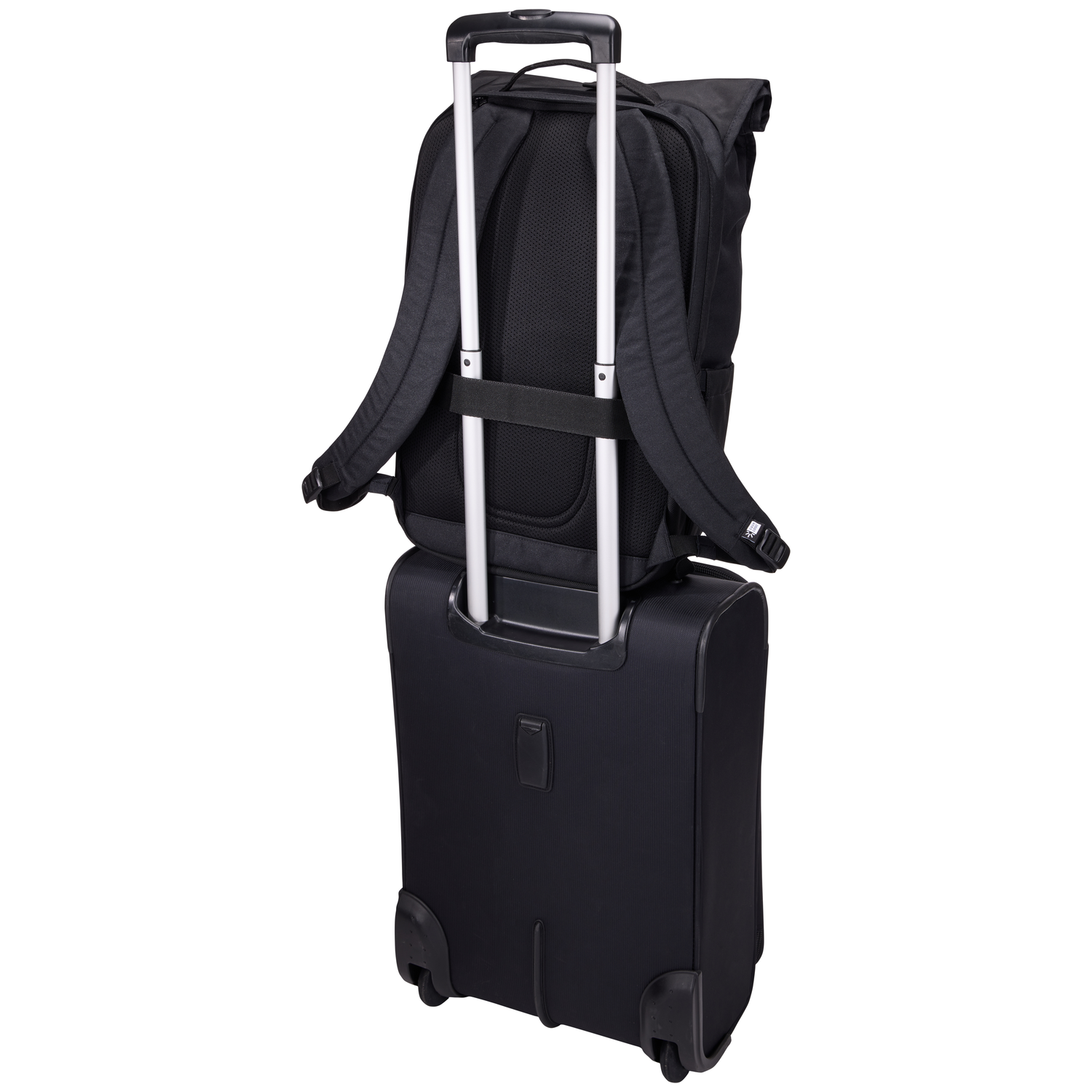 A black backpack is placed on a black rolling suitcase. The backpack has straps. The suitcase has wheels and a handle.