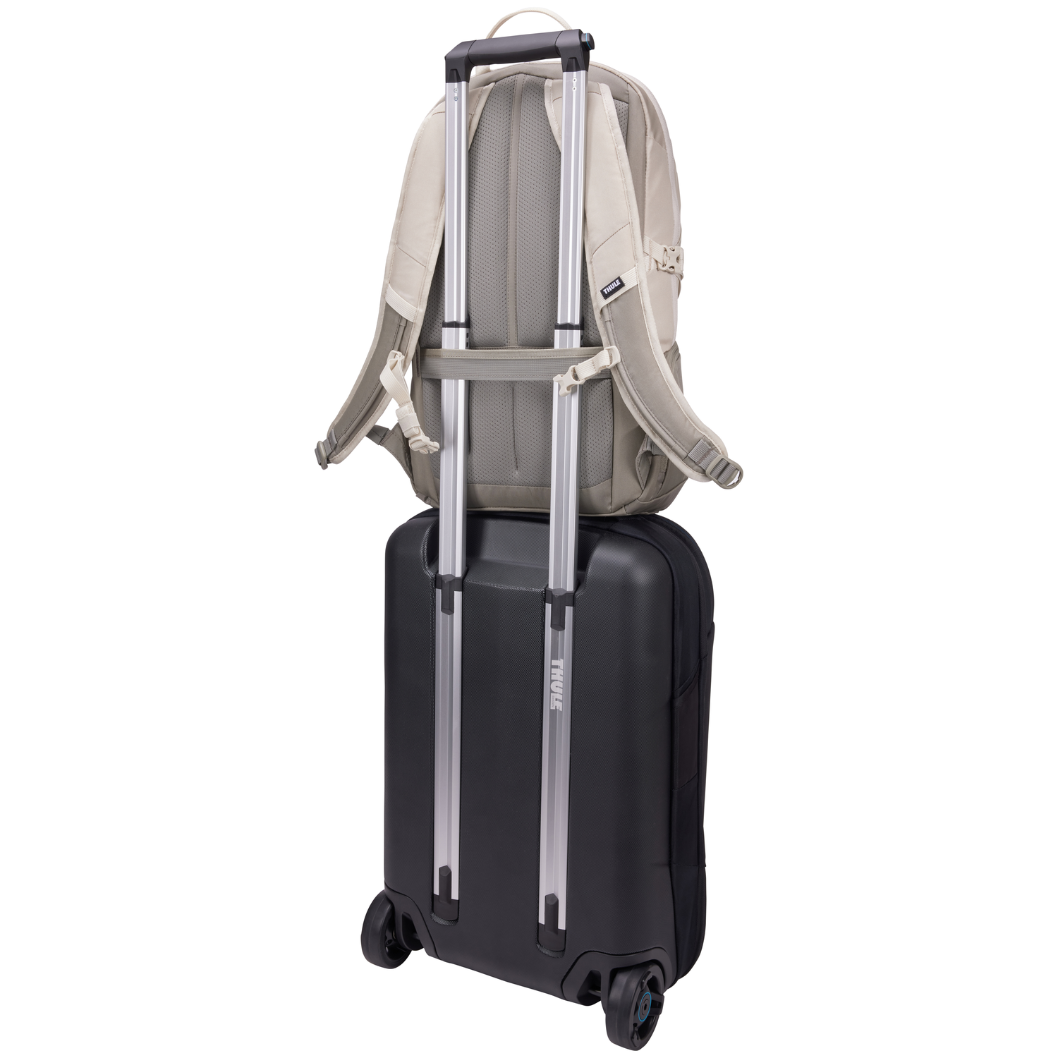 A beige backpack rests on a black rolling suitcase. Both are against a white background.