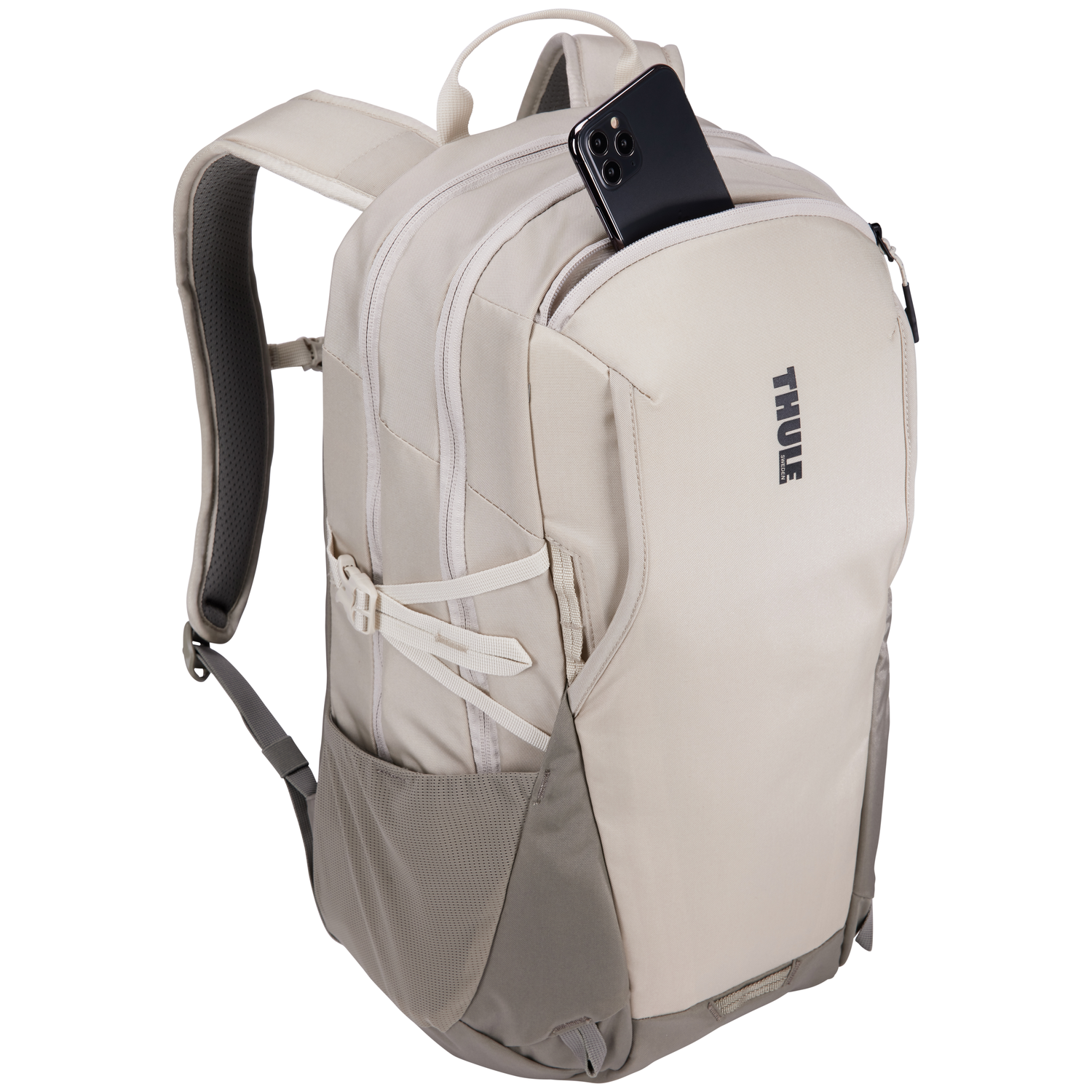 A beige Thule backpack with a phone in the front pocket. The backpack has adjustable straps and a handle. The background is white.