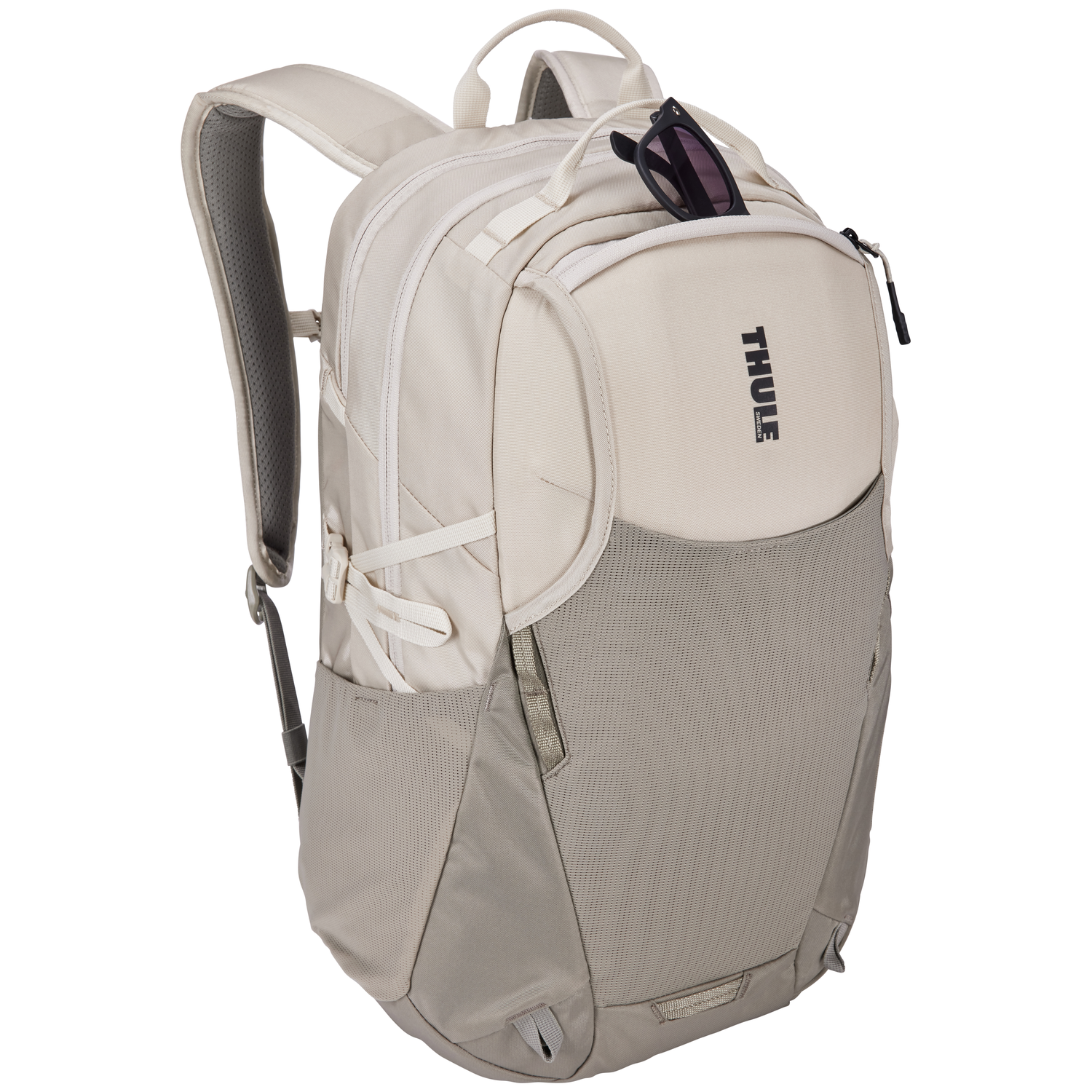 Beige backpack with sunglasses. Gray mesh pocket on the bottom. Black 'THULE' logo. White straps and zipper.
