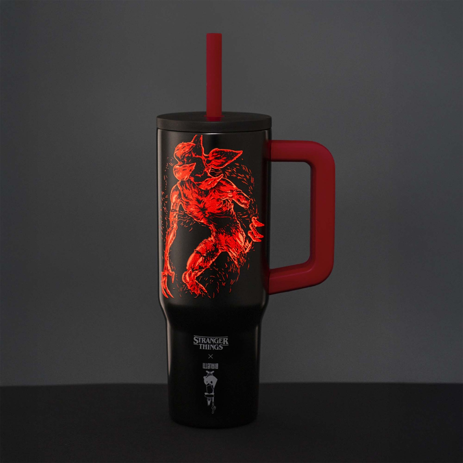 Tazza nera di Stranger Things con manico rosso, design. Cannuccia rossa. Il design mostra un Demogorgon rosso. Lo sfondo è grigio scuro.