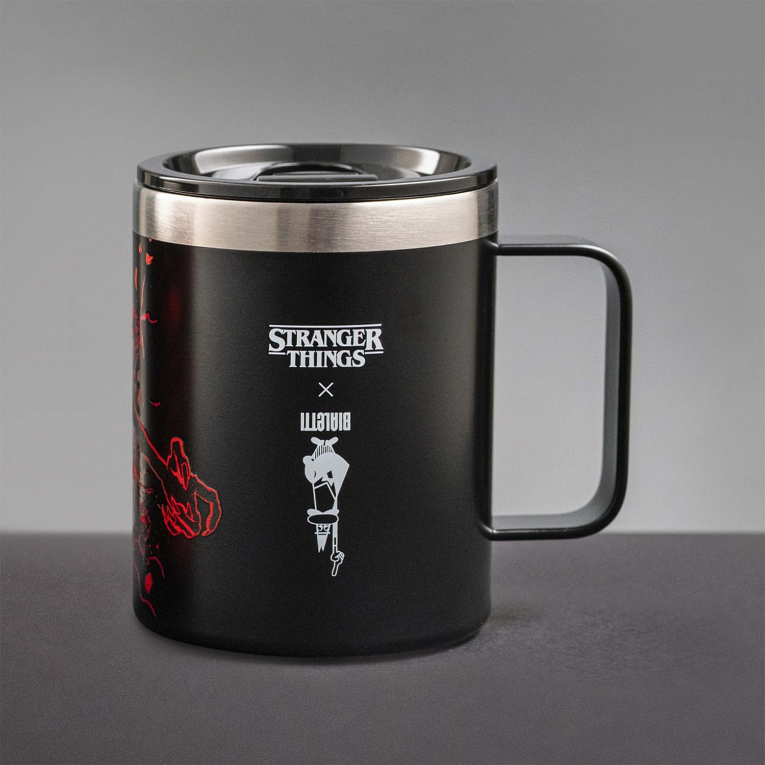 Tazza nera di Stranger Things con manico e coperchio. Presenta il logo di Stranger Things e una grafica rossa sul lato.