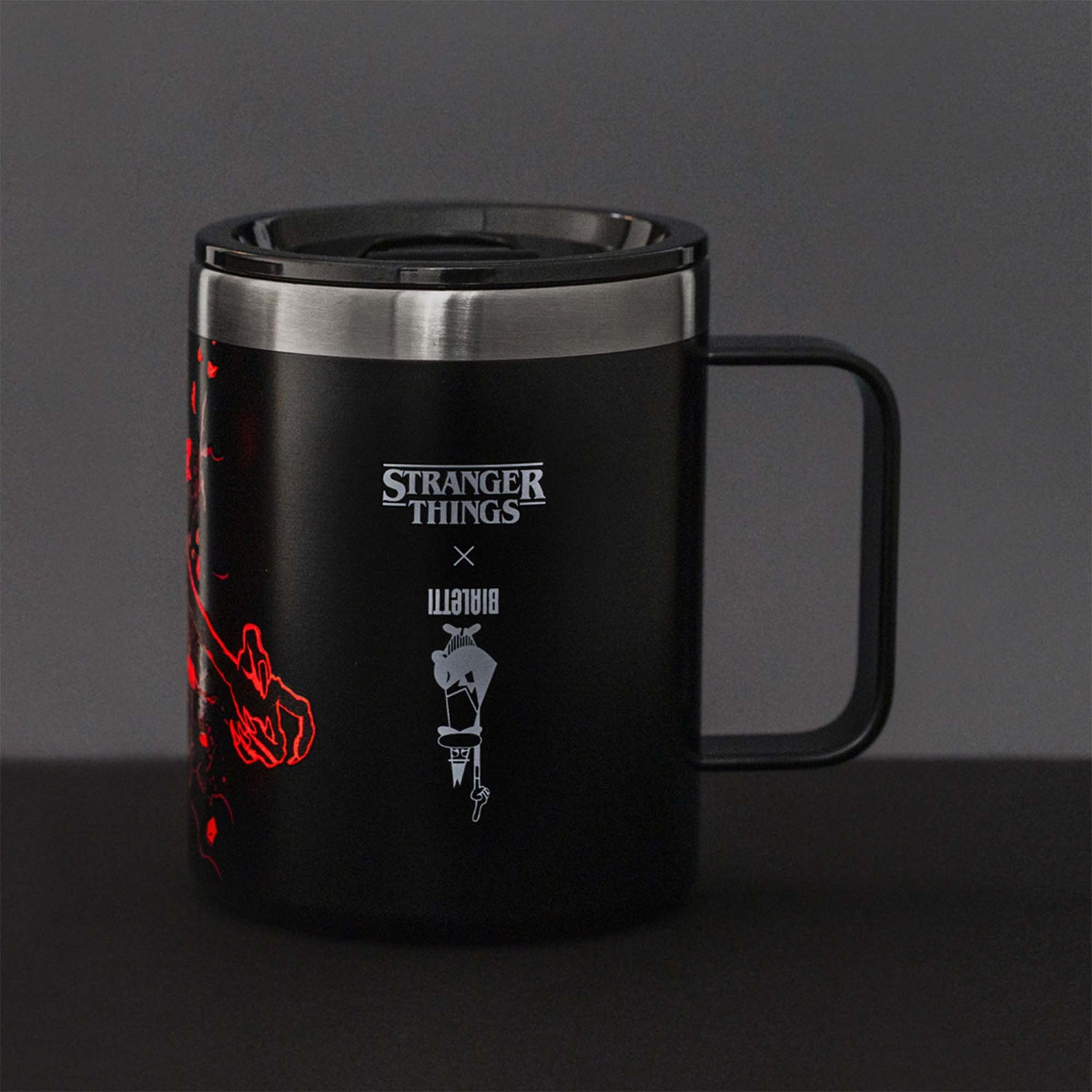 Tazza nera di Stranger Things con logo, grafica rossa e bordo argentato, manico a destra, su una superficie scura.