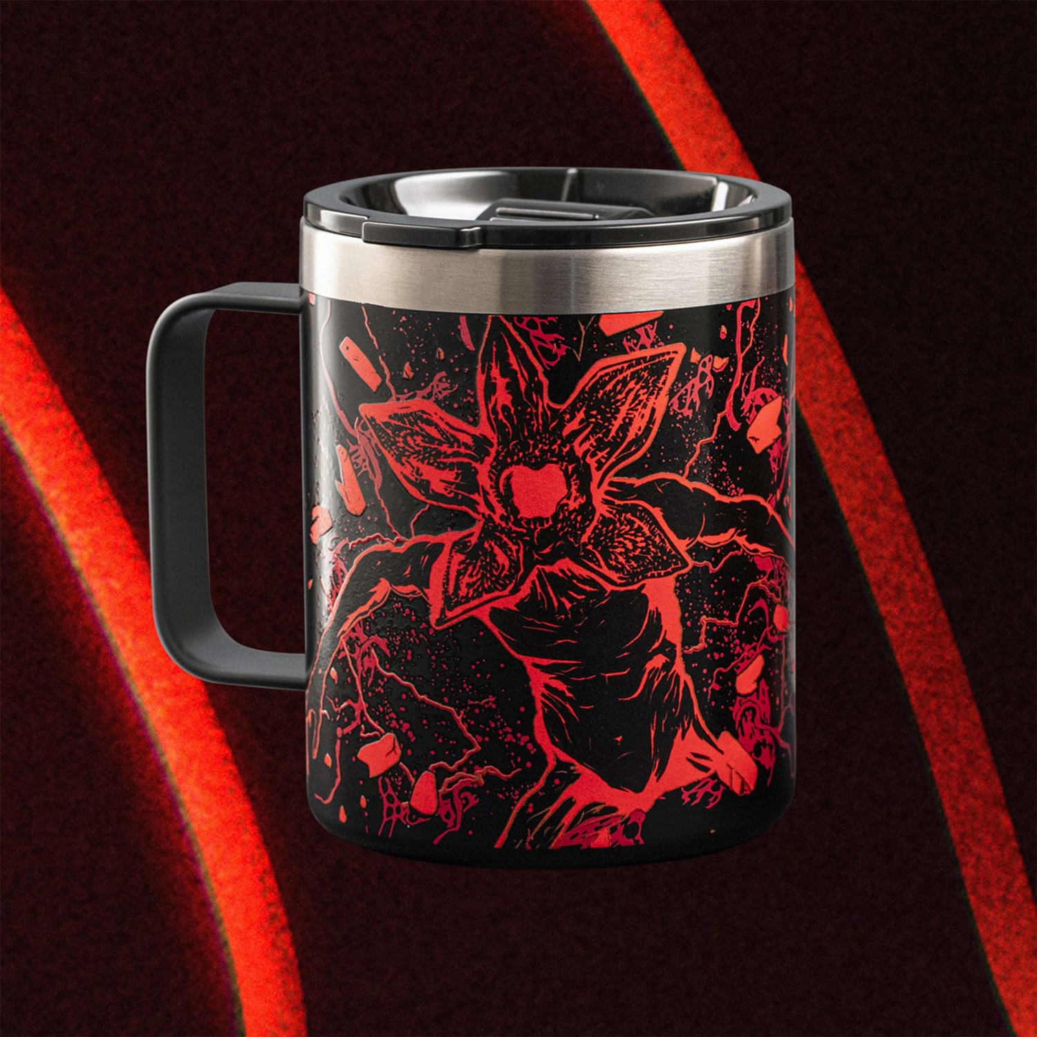 Un bicchiere da viaggio nero con un design Demogorgon rosso. Lo sfondo è rosso scuro con una striscia rossa più chiara a destra.