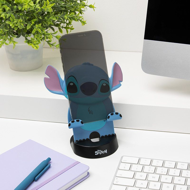 A Stitch telefontartó egy telefont tart. Zöld növény, lila jegyzetfüzet és billentyűzet is található egy fehér asztalon.