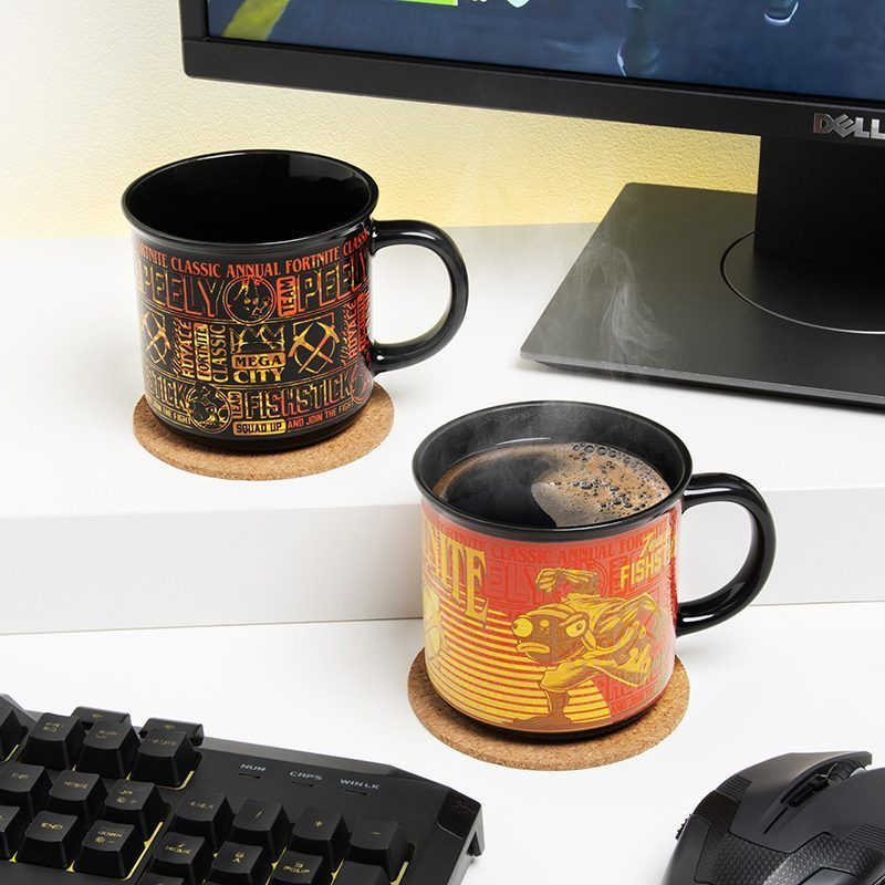 Két fekete bögre Fortnite dizájnnal alátéteken, gőz száll fel az egyikből. A háttérben egy billentyűzet, egér és monitor látható.