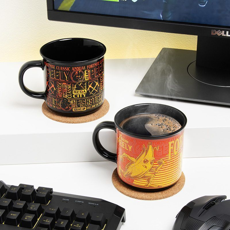 Két fekete bögre Fortnite mintákkal alátéteken, egy billentyűzet, egér és számítógép monitor közelében. Az egyik gőzöl.