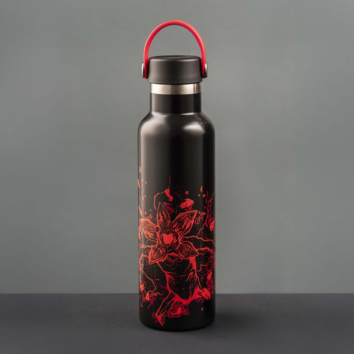 Borraccia nera con disegno rosso a forma di fiore. Ha un manico rosso, tappo nero e anello argentato.