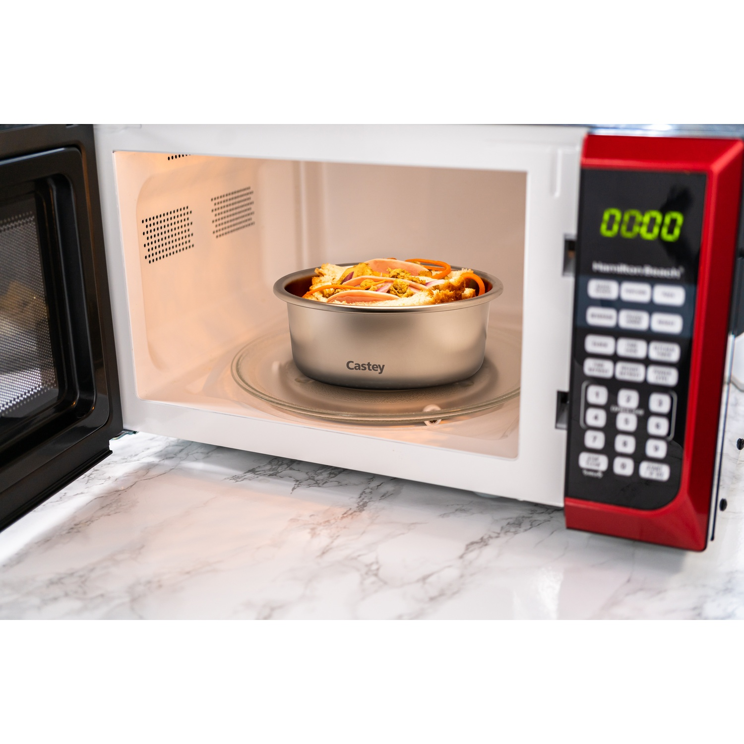 Un forno a microonde aperto con cibo all'interno. Una ciotola di cibo su un piatto di vetro.