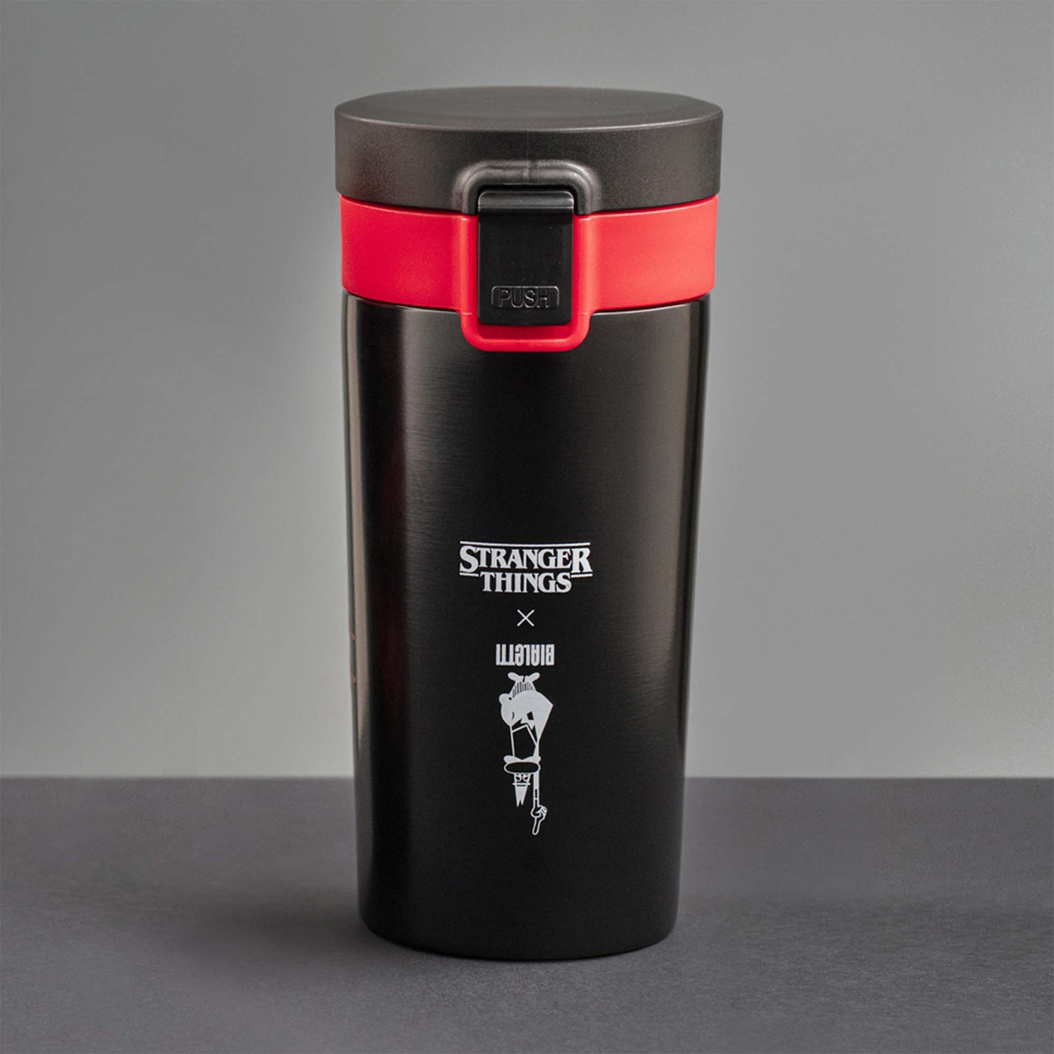Tazza da viaggio nera di Stranger Things con fascia rossa e coperchio nero. Il logo dice 'Stranger Things x Bialetti' con una grafica.