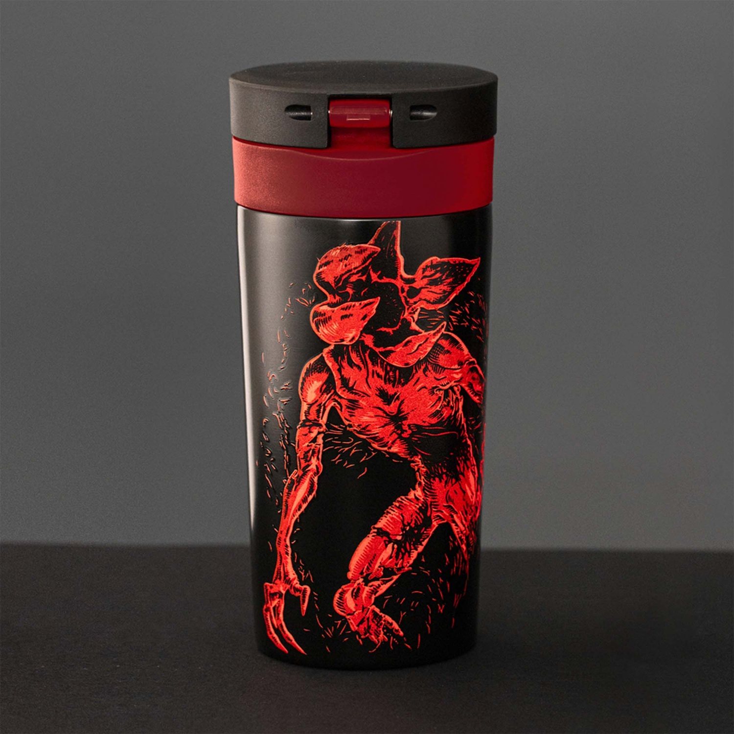 Tazza da viaggio nera con illustrazione rossa del Demogorgon. Il coperchio è nero, con fascia rossa. Lo sfondo è grigio scuro, superficie nera.