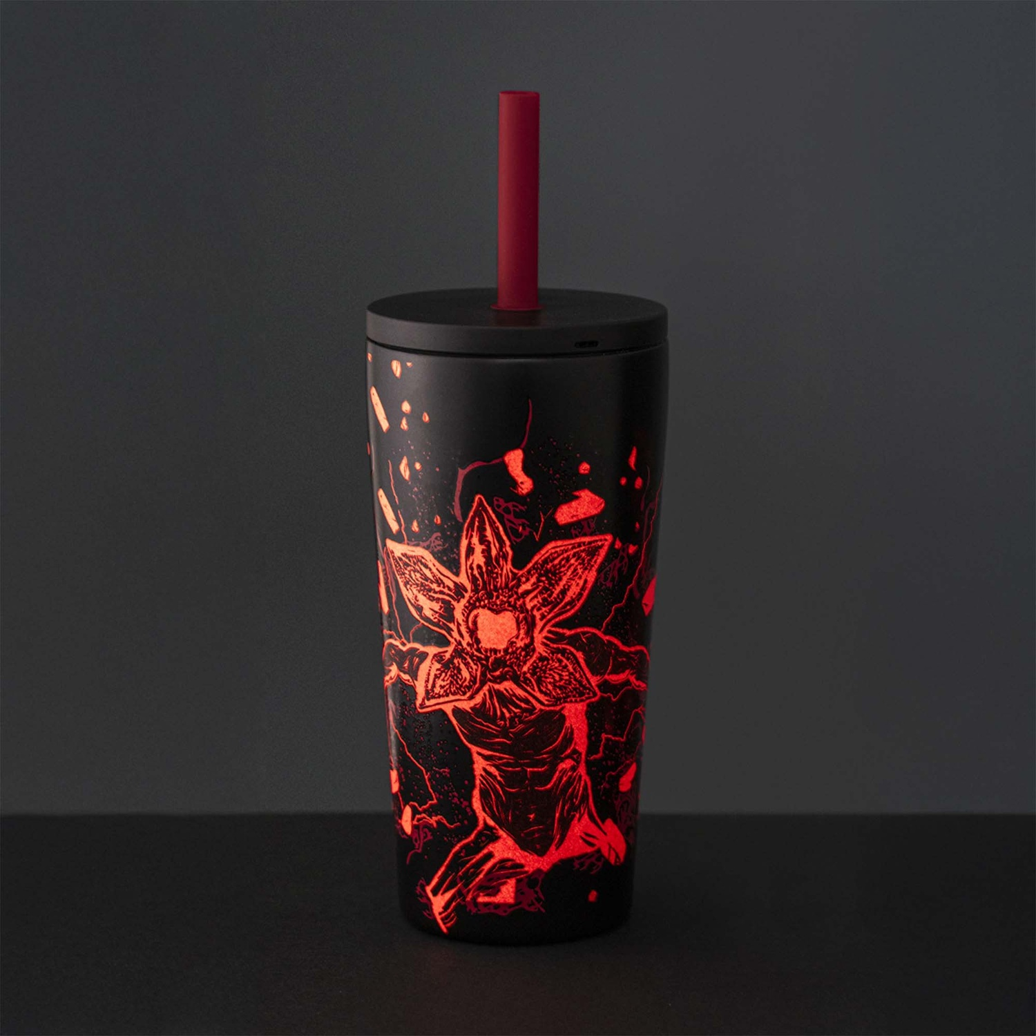 Bicchiere nero con design Demogorgon rosso brillante, cannuccia rossa e coperchio nero. Sfondo scuro.