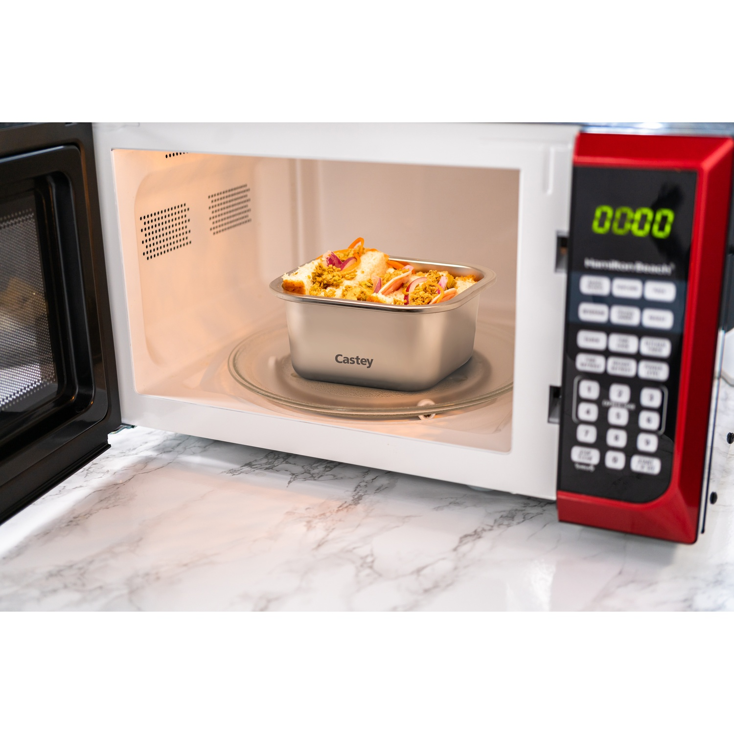 Cibo in un contenitore di metallo all'interno di un forno a microonde. Il forno a microonde è aperto. Il forno a microonde ha un pannello di controllo rosso.