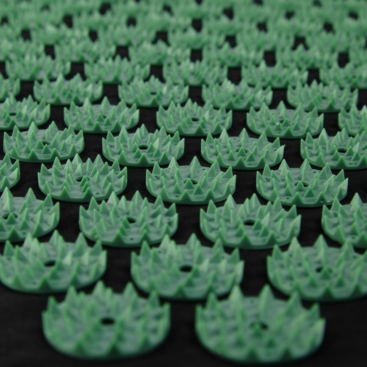 Zbliżenie zielonej maty do akupresury z wieloma małymi, kolczastymi punktami ułożonymi w siatkę na czarnej powierzchni.