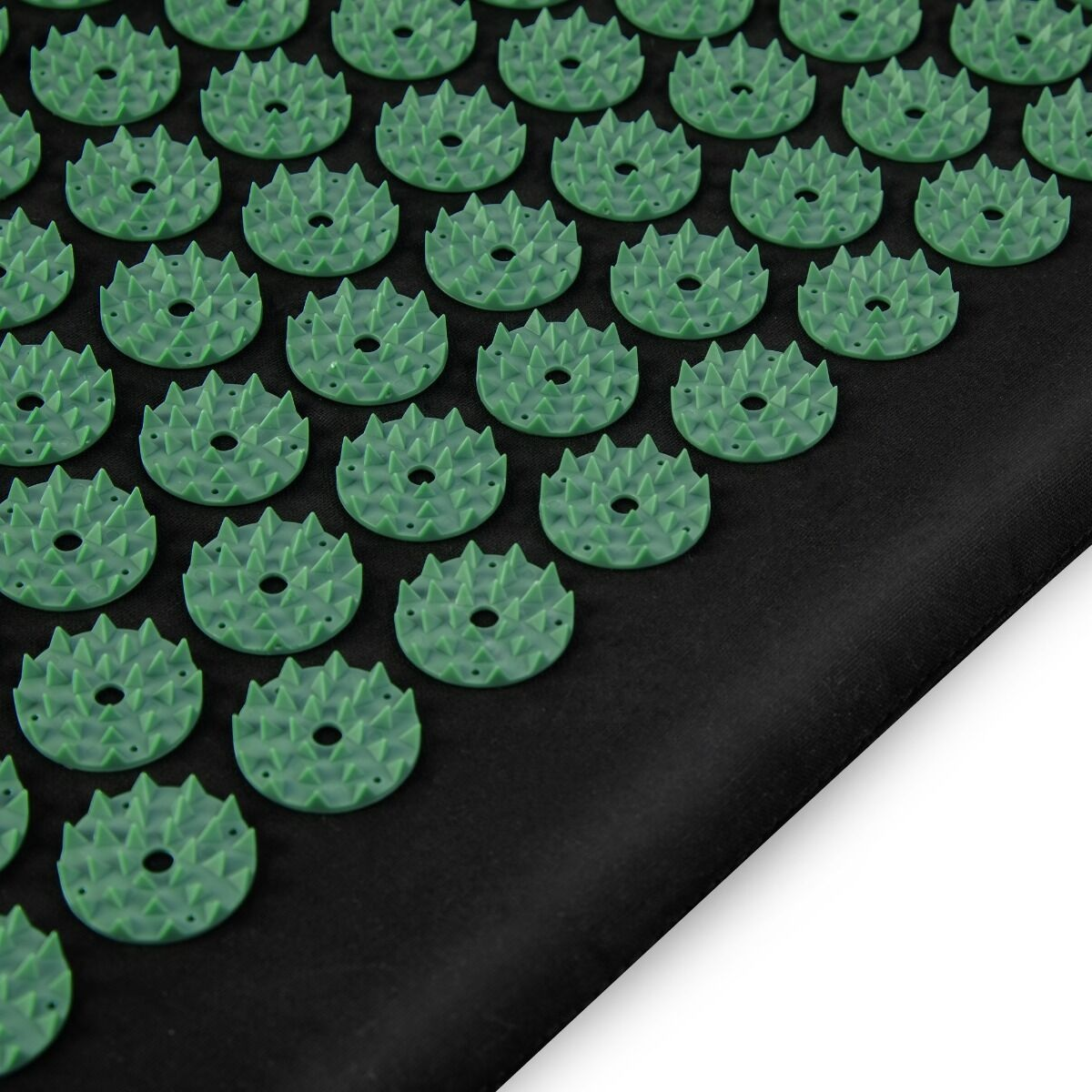 Zielona plastikowa mata do akupresury z zaokrąglonymi kolcami na czarnym tle z tkaniny. Białe tło po prawej stronie.