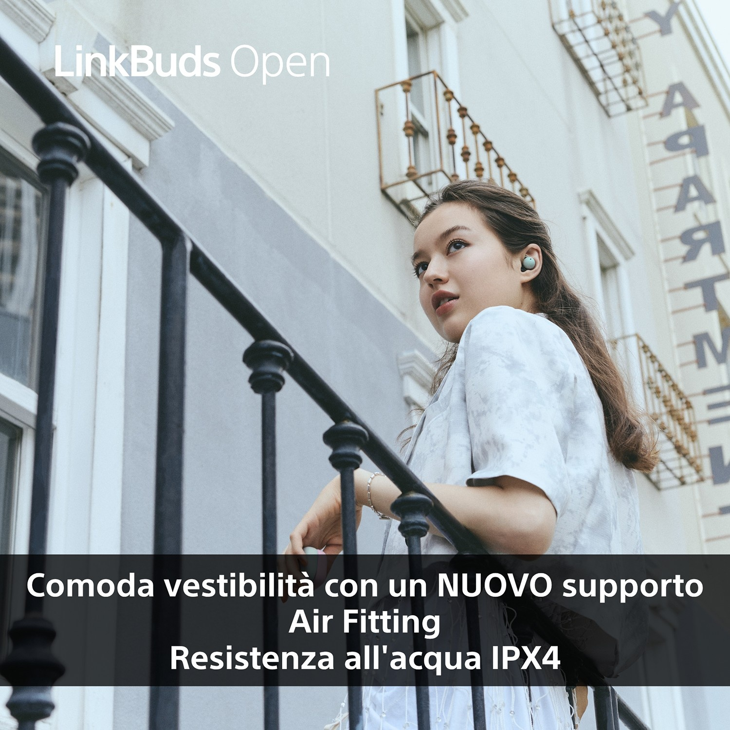 Una giovane donna con auricolari guarda in alto. È su un balcone. Testo: 'Vestibilità confortevole con NUOVO Air Fitting, resistenza all'acqua IPX4'.