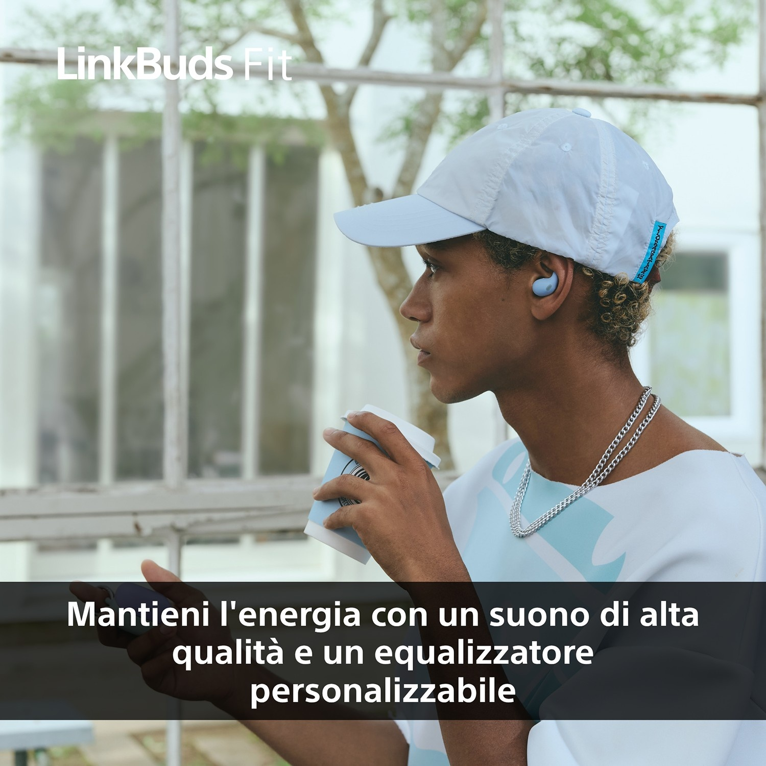 Una persona con berretto e auricolari, che tiene in mano una tazza di caffè. Lo sfondo mostra una finestra e il testo LinkBuds Fit.