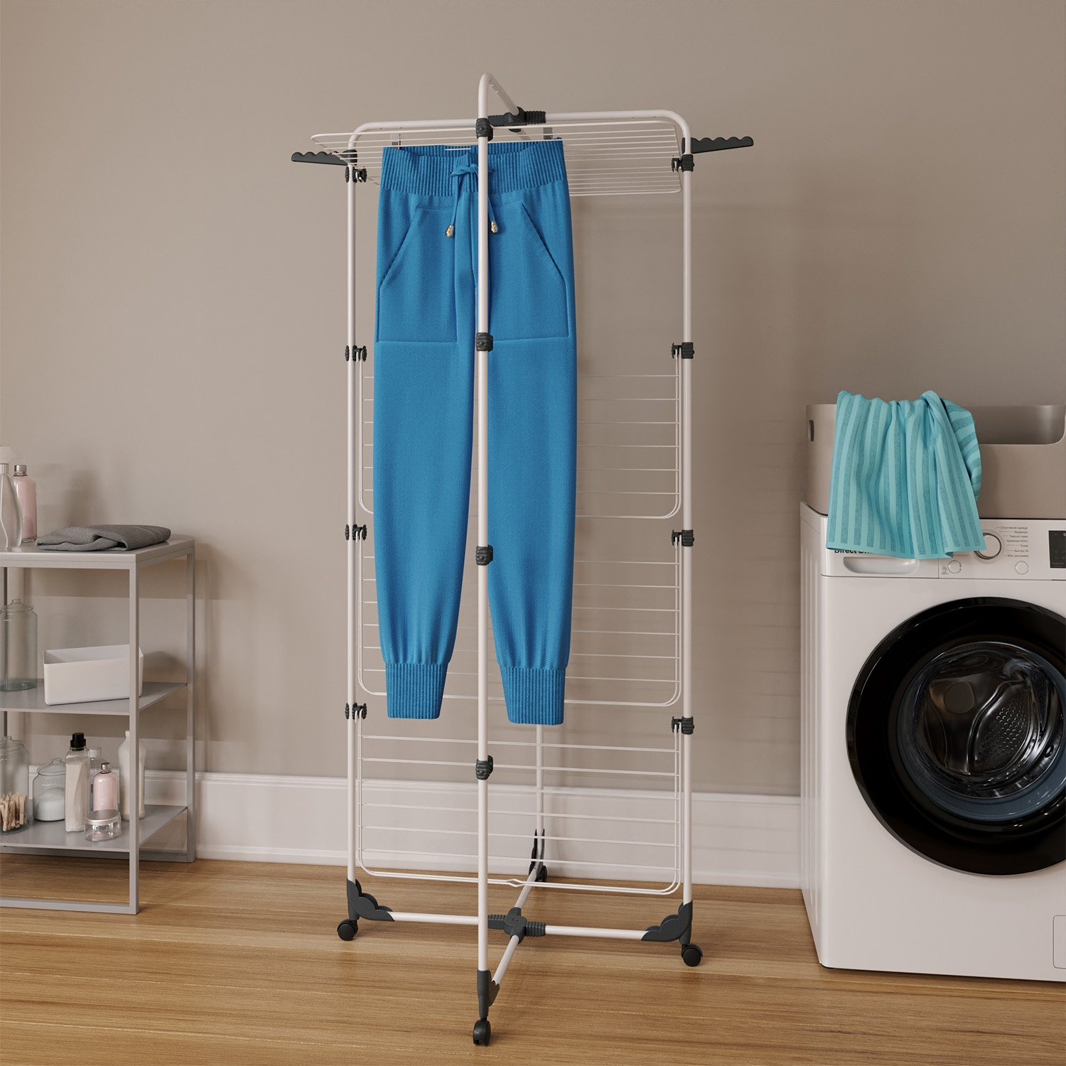 Pantaloni della tuta blu appesi a un stendino bianco. Una lavatrice a destra. Scaffali con bottiglie a sinistra.