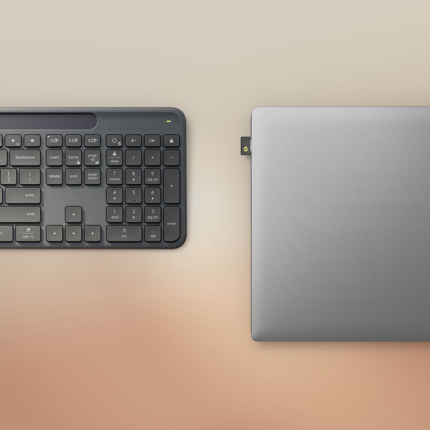 Una tastiera grigia e un laptop argentato sono posizionati su una superficie beige. La tastiera ha vari tasti funzione.