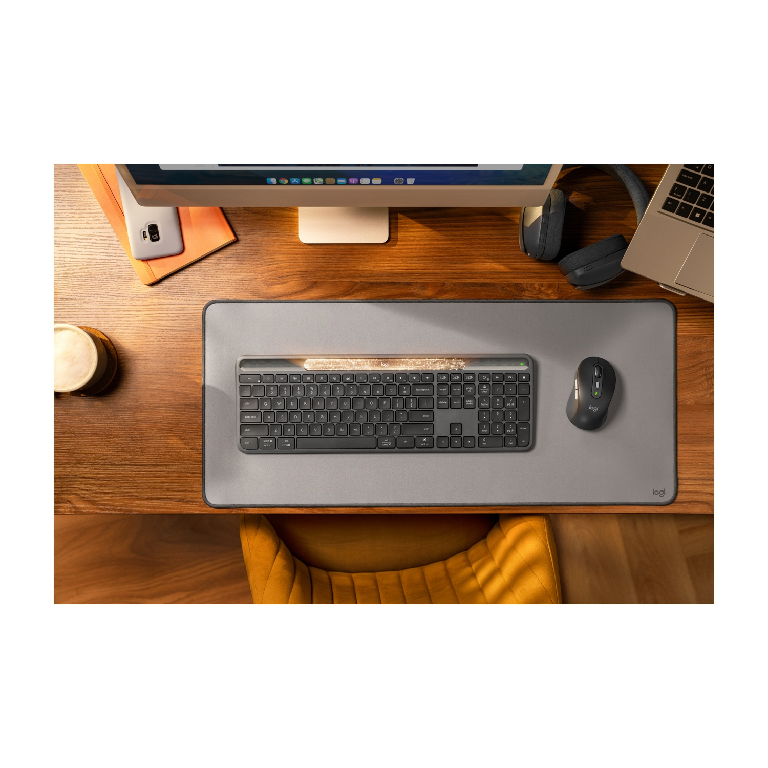 Configurazione scrivania con tastiera, mouse, cuffie, laptop e monitor. Sono presenti anche un telefono e una tazza di caffè.
