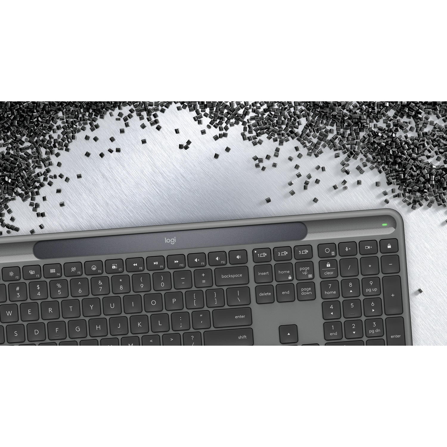 Una tastiera Logitech su una superficie metallica, circondata da piccoli oggetti rettangolari scuri.