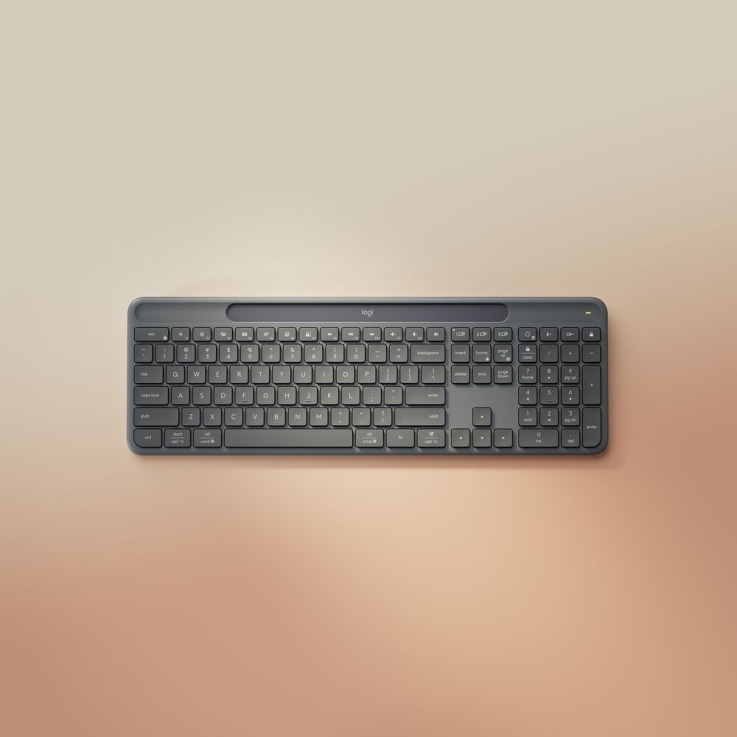 Vista dall'alto di una tastiera Logitech grigio scuro su uno sfondo beige sfumato. La tastiera ha un tastierino numerico.