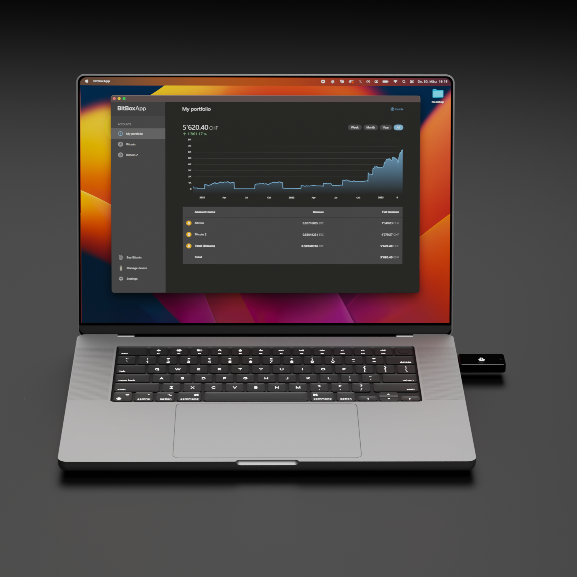 Laptop zeigt BitBoxApp-Portfolio. Es zeigt ein Diagramm und Kontodetails mit Bitcoin-Werten. Ein schwarzes Gerät liegt rechts.