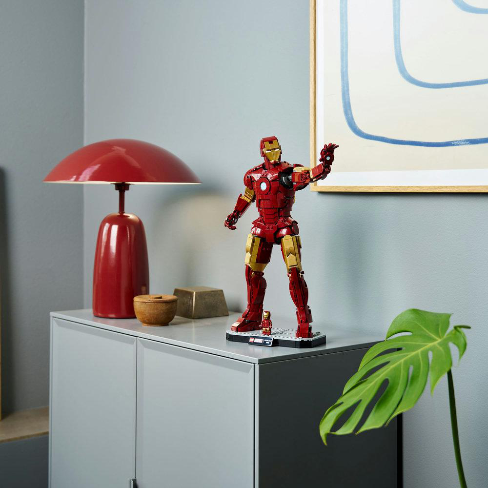 Iron Man Lego Figur auf einem grauen Schrank mit roter Lampe. Ein Monstera-Blatt ist im Vordergrund. Im Hintergrund hängt ein Bild.