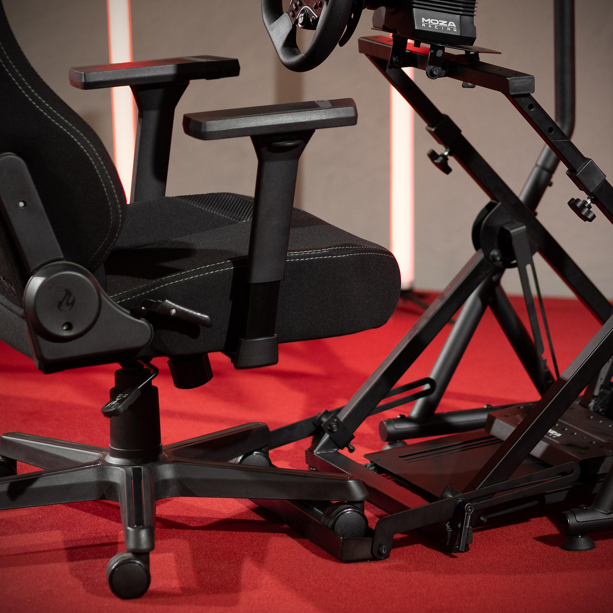 Gaming-Setup. Schwarzer Stuhl, Lenkrad und Metallrahmen auf rotem Teppich. MOZA Racing-Logo sichtbar.