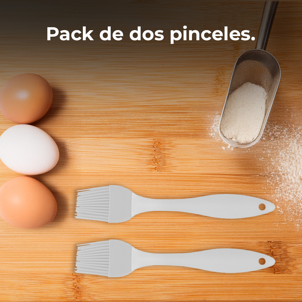 Dos pinceles grises, tres huevos y harina sobre una superficie de madera. Una cuchara con harina está arriba a la derecha.