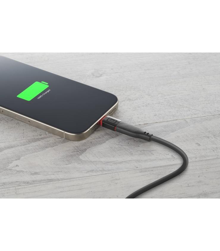 Un teléfono cargando, mostrando 100% cargado. Cable negro enchufado. El teléfono es dorado y negro. El fondo es una mesa de madera.