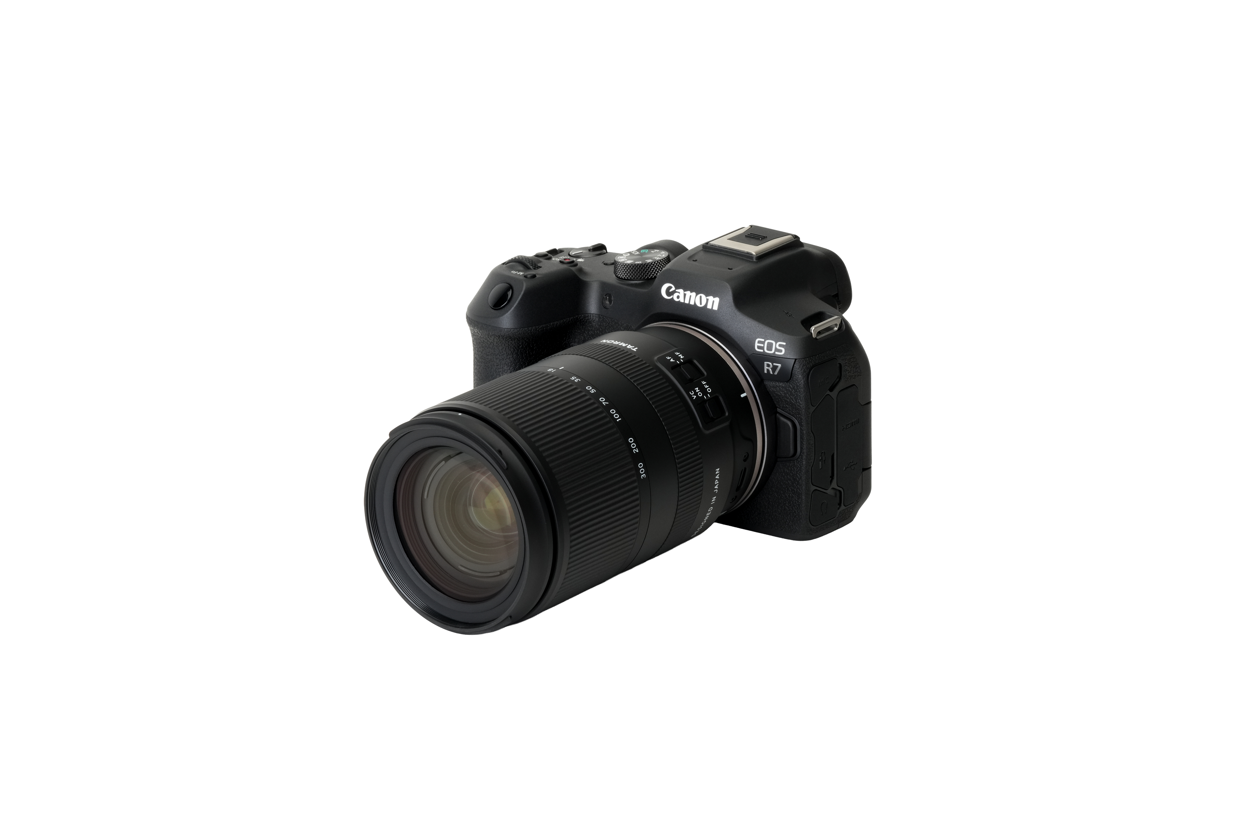 Eine schwarze Canon EOS R7 Kamera mit einem Tamron-Objektiv auf weißem Hintergrund. Das Objektiv ist am Kameragehäuse befestigt.