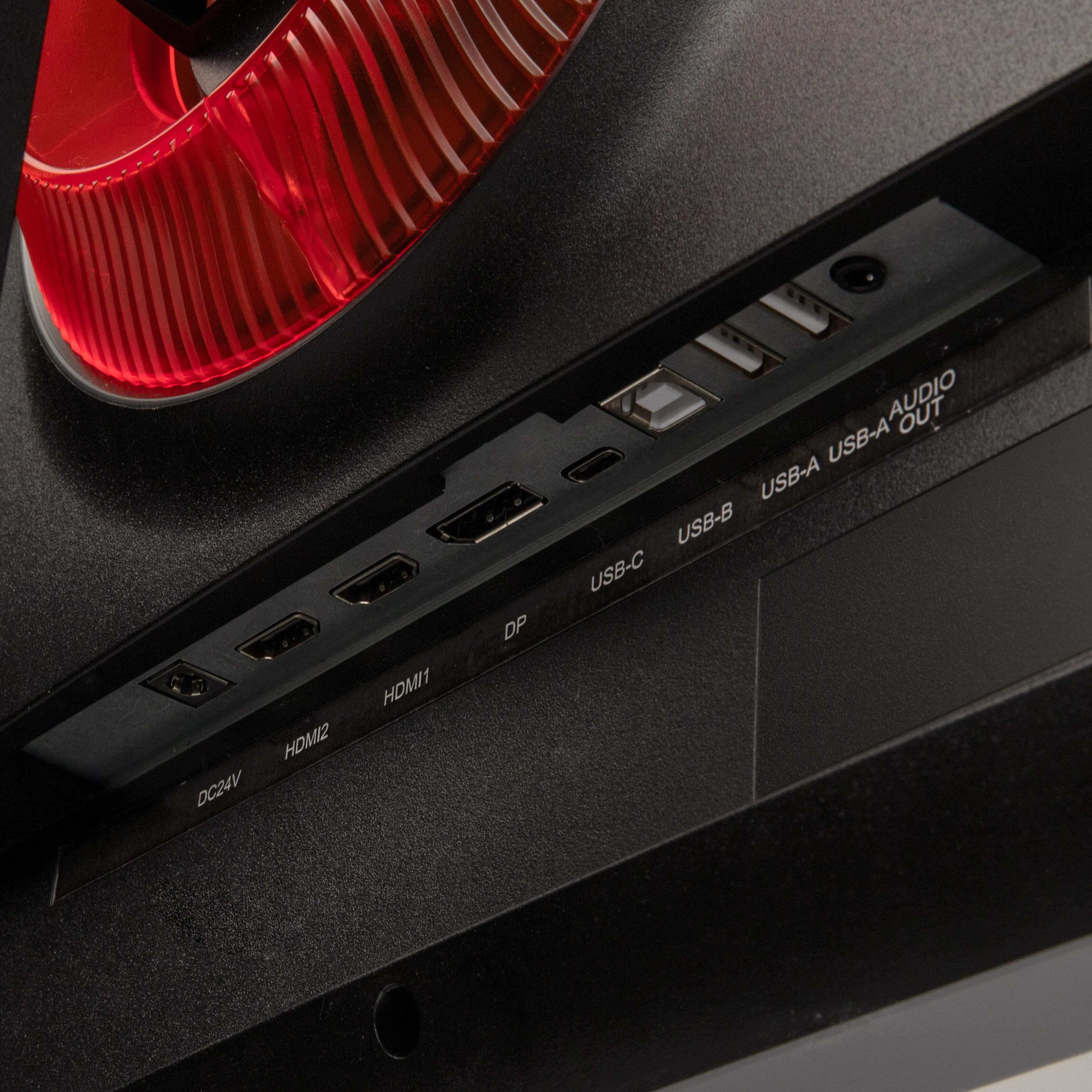 Nahaufnahme der Rückseite eines Monitors mit Anschlüssen: HDMI, USB und Audioausgang. Roter Kunststoff und schwarze Textur.