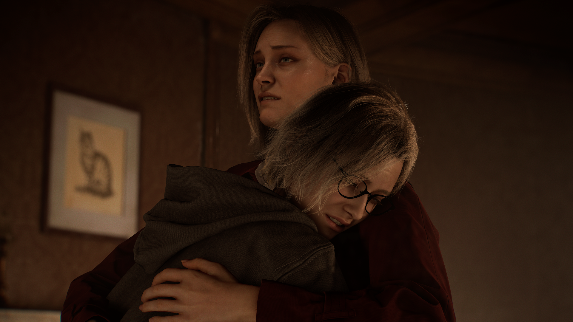 Dwie kobiety się obejmują. Jedna nosi okulary i bluzę z kapturem, druga czerwoną koszulę. W tle wisi obraz. Obie wyglądają na smutne.