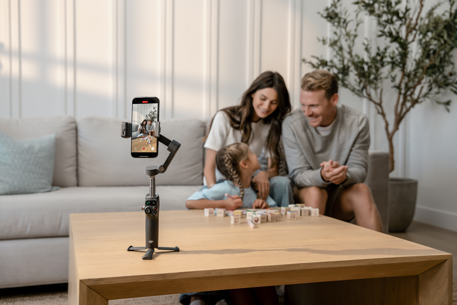 Familia grabando un video. Un teléfono en un trípode captura a una familia. Juegan con bloques en una mesa de madera.