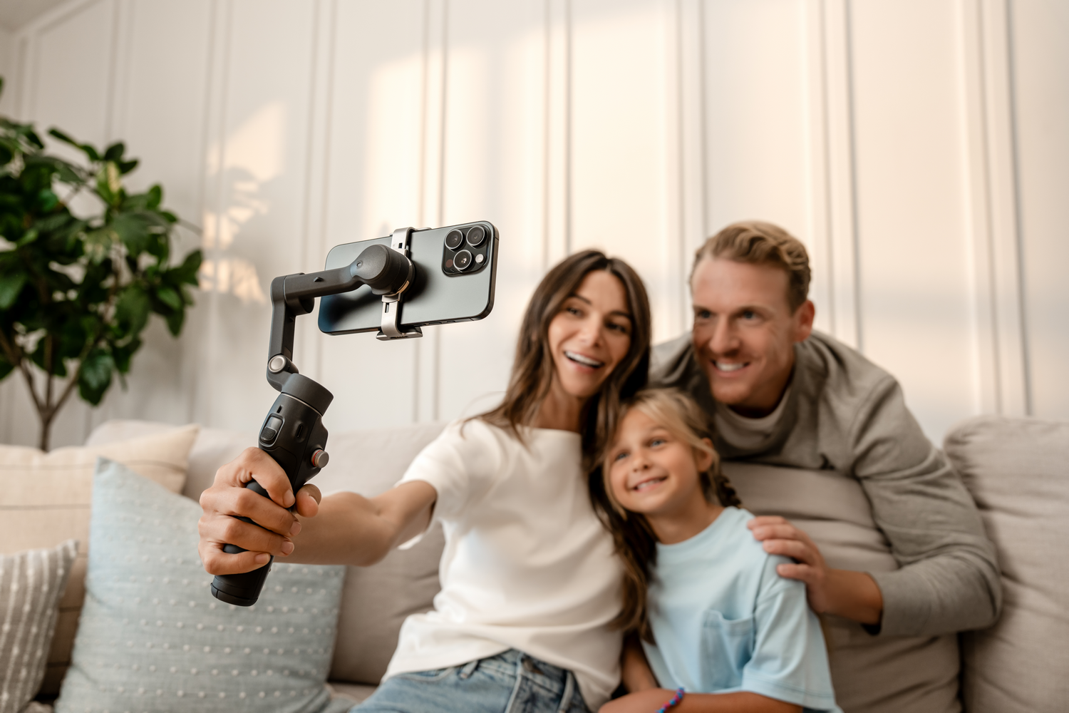 Familia tomándose una selfie con un teléfono en un cardán. Mujer sosteniendo el cardán, sonriendo con un hombre y un niño.