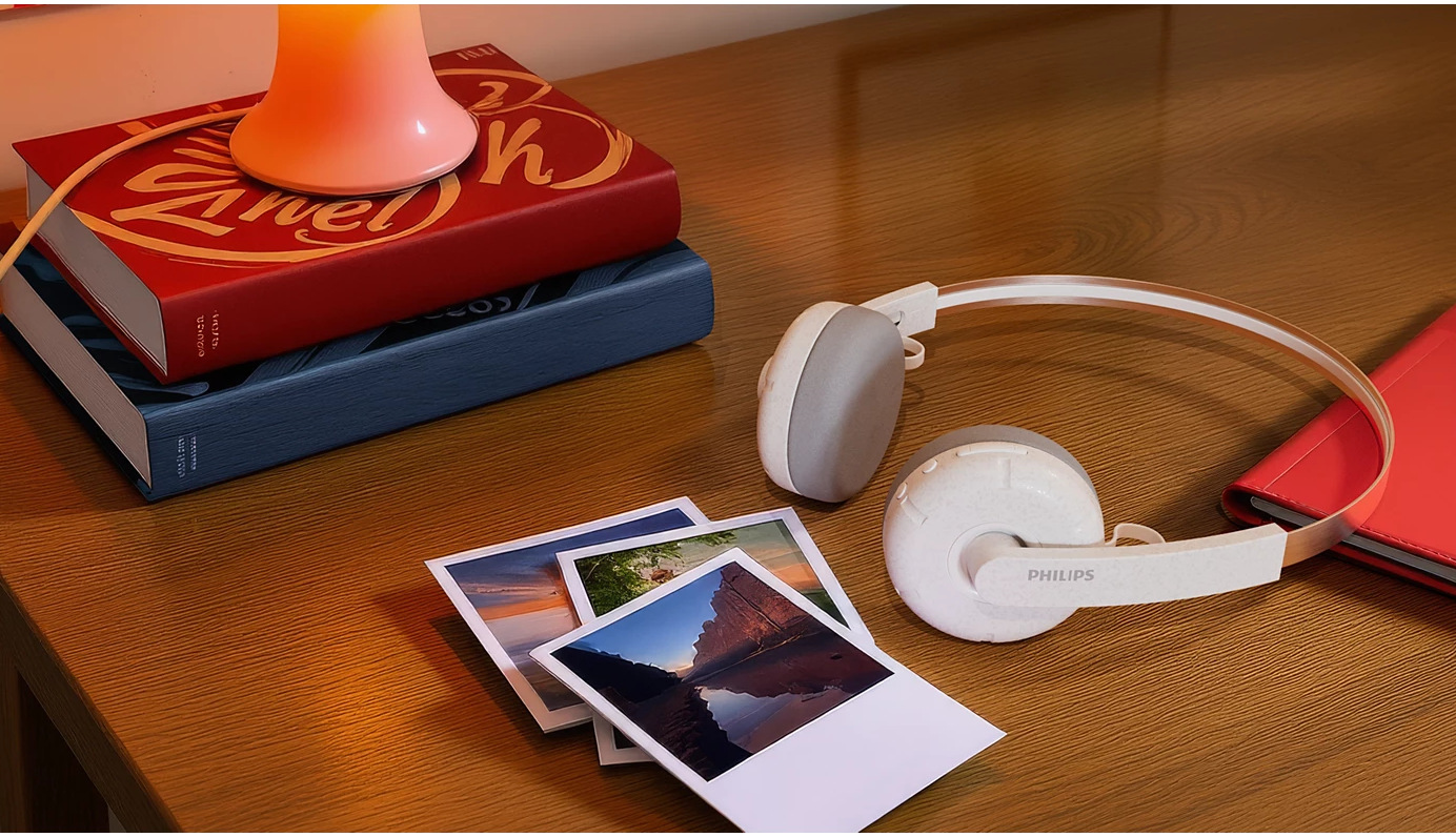 Biurko z książkami, lampą, słuchawkami i zdjęciami. Dominują kolory czerwony, niebieski i biały. Widoczne słuchawki Philips.