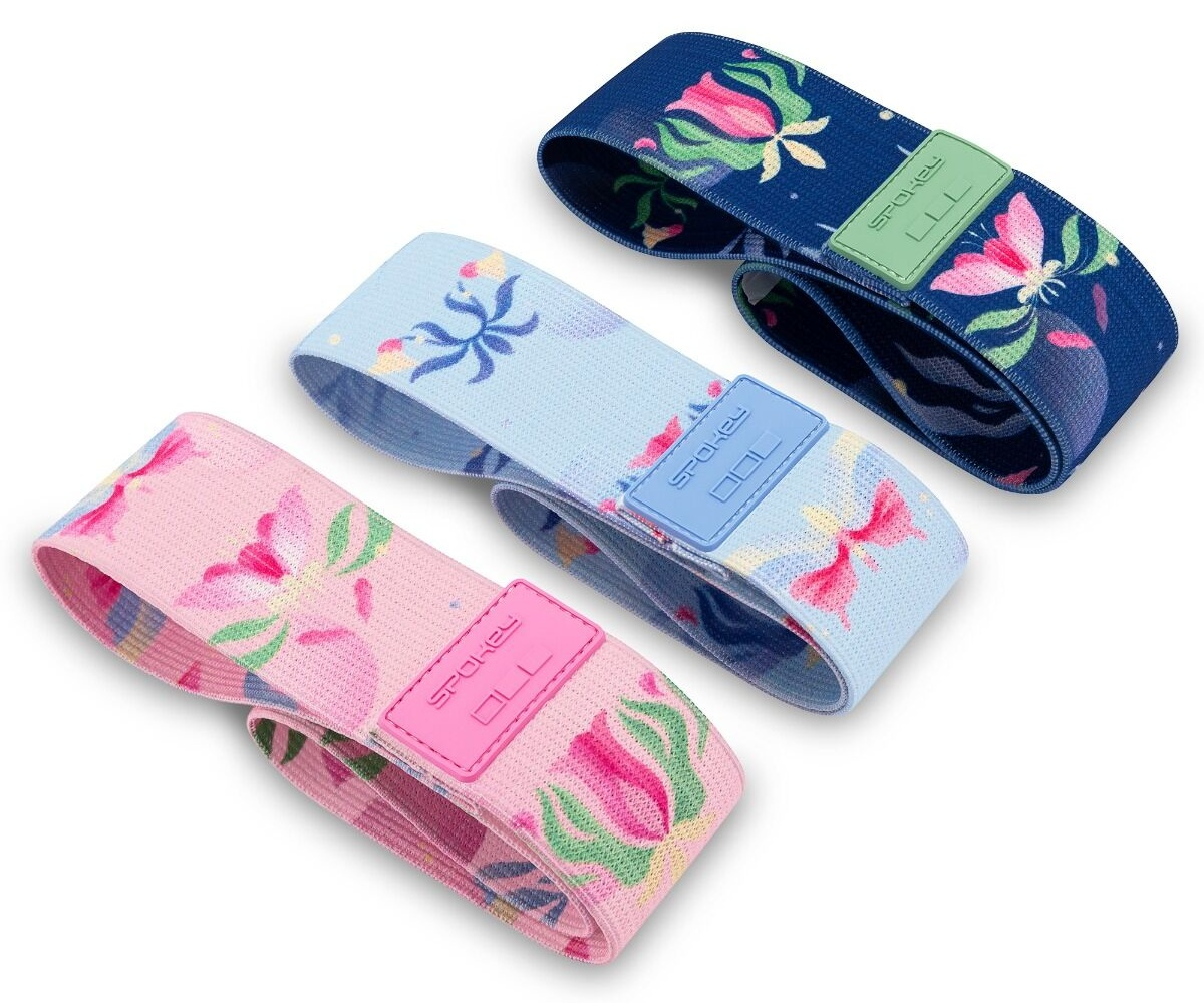 Trzy kwiatowe opaski oporowe w kolorze różowym, jasnoniebieskim i granatowym. Każda ma kolorową etykietę z nazwą marki. Białe tło.